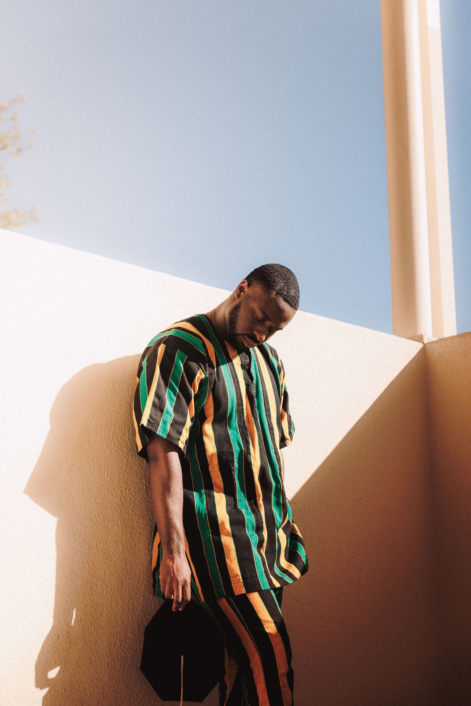 Person in striped shirt standing against a wall casting dramatic shadows in natural sunlight.