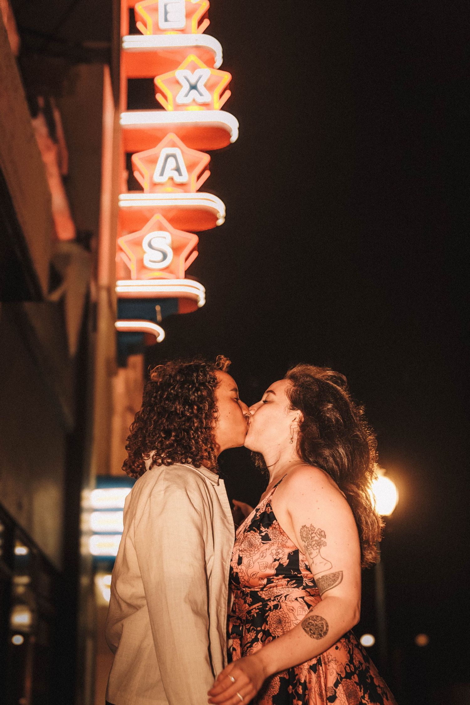 Couple shares a romantic kiss under a glowing Texas neon theater sign at night.