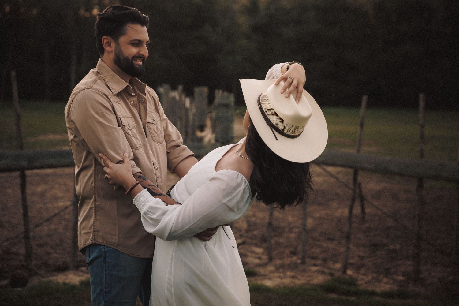 Playful couple dancing outdoors with woman wearing a cowboy hat at dusk.
