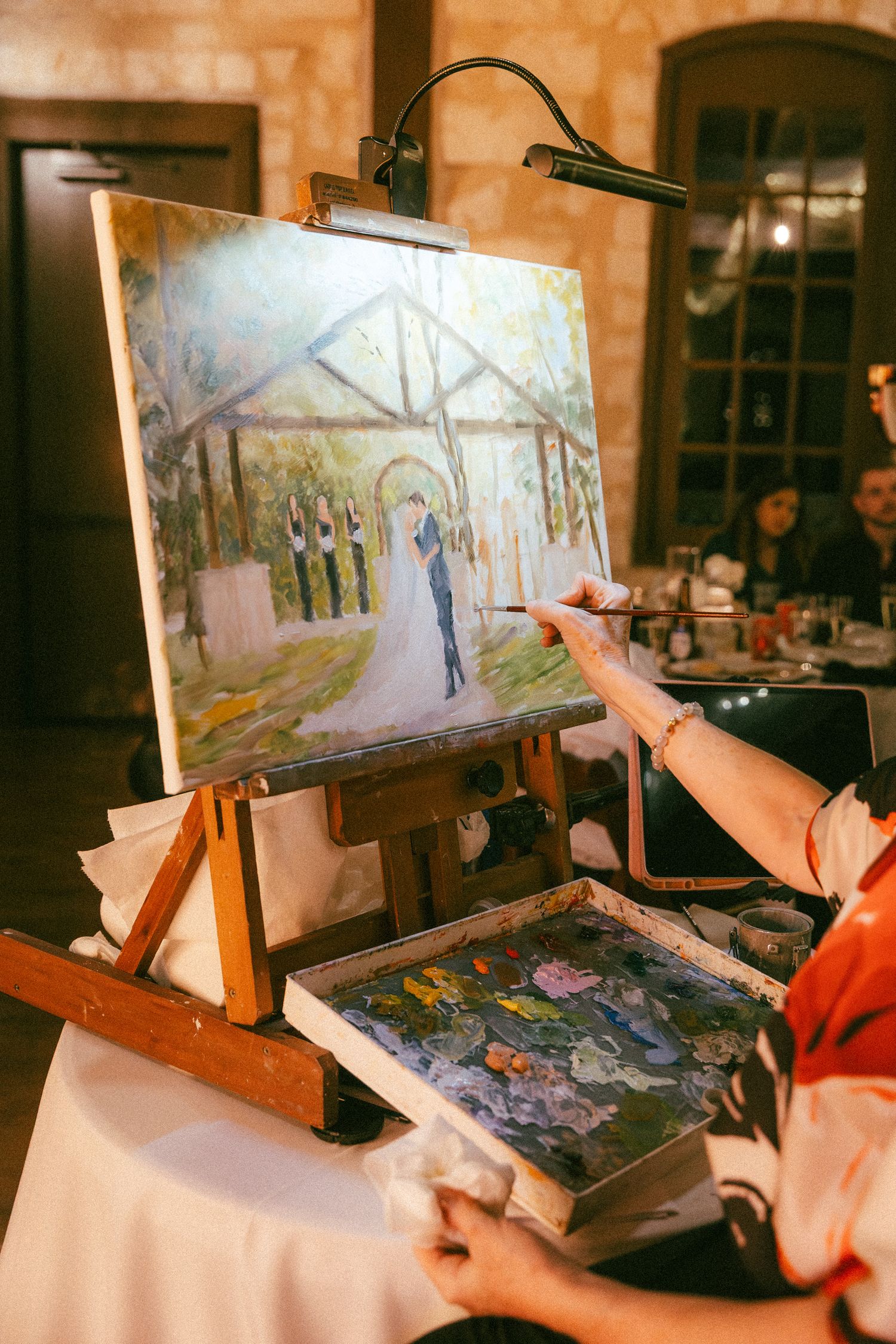 An artist paints a live wedding portrait on an easel depicting the bride and groom at the altar during the reception.