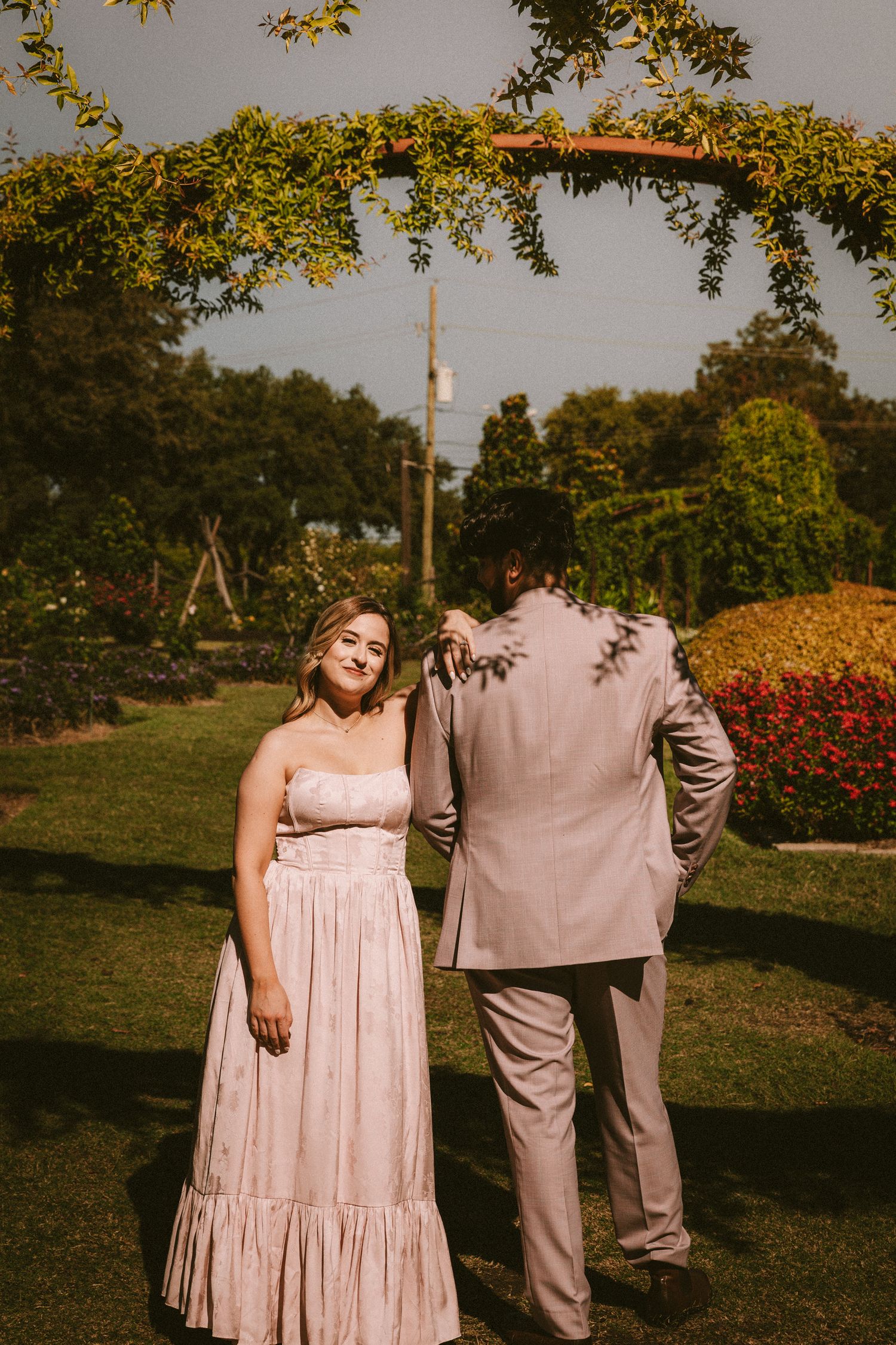 Couple in coordinated pink and beige outfits standing together in a garden setting.