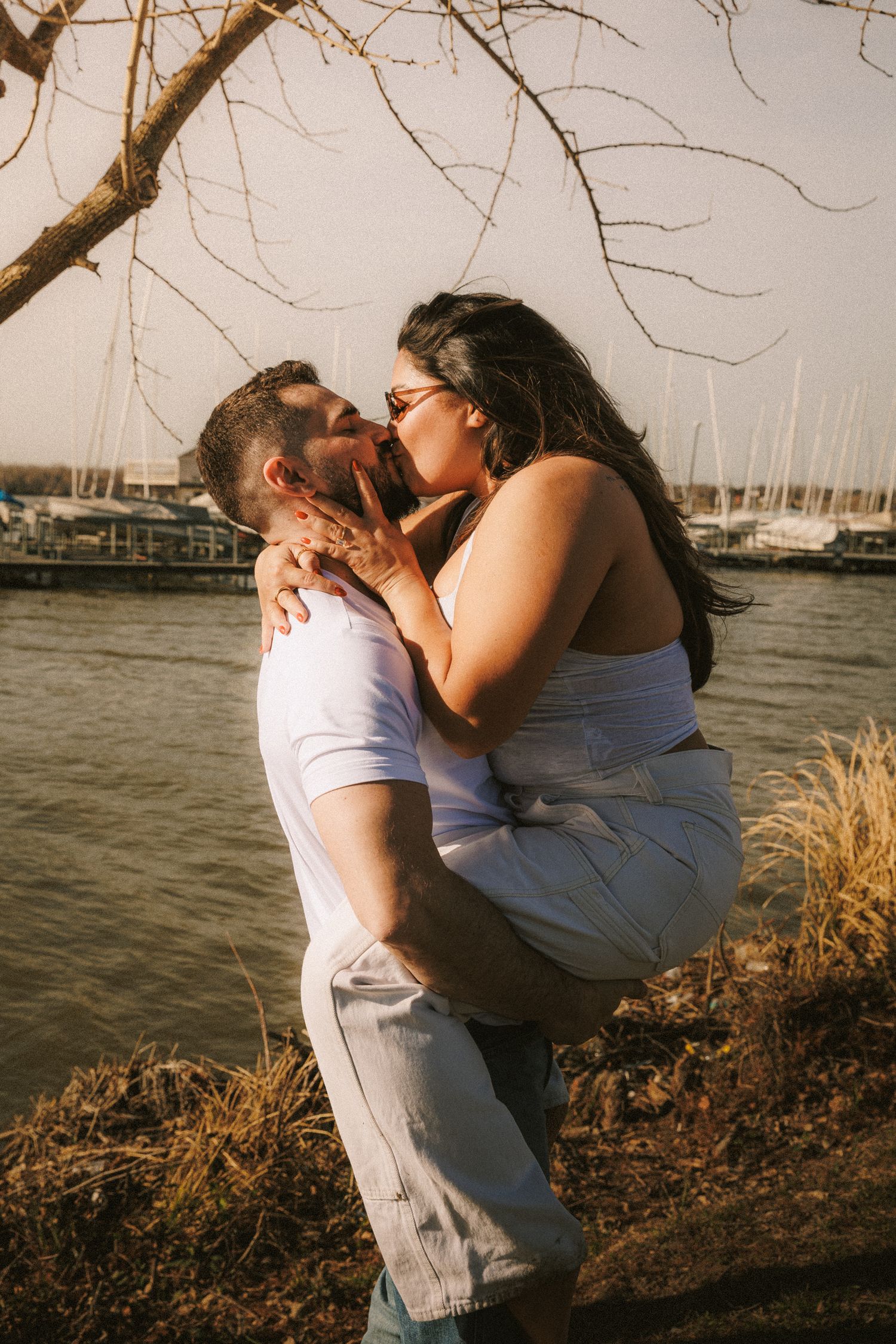 Couple shares playful embraces by the waterfront during a sunset photo session.