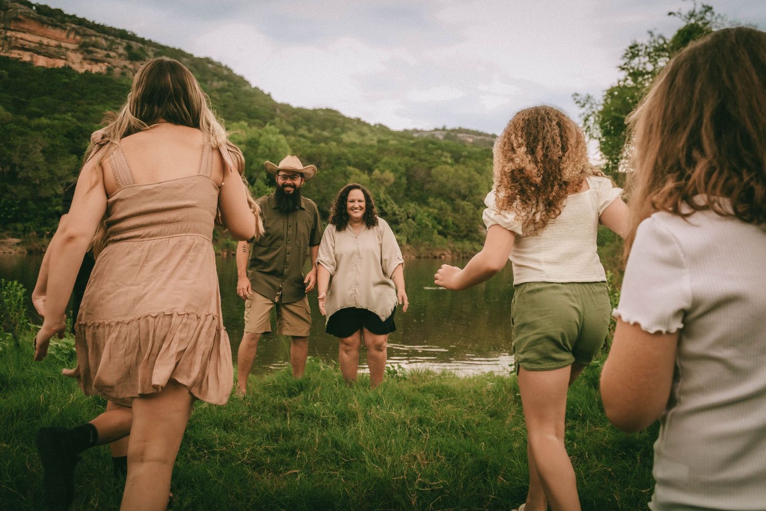 Friends enjoying a fun photo session in casual attire walking along a scenic hillside path near a lake.