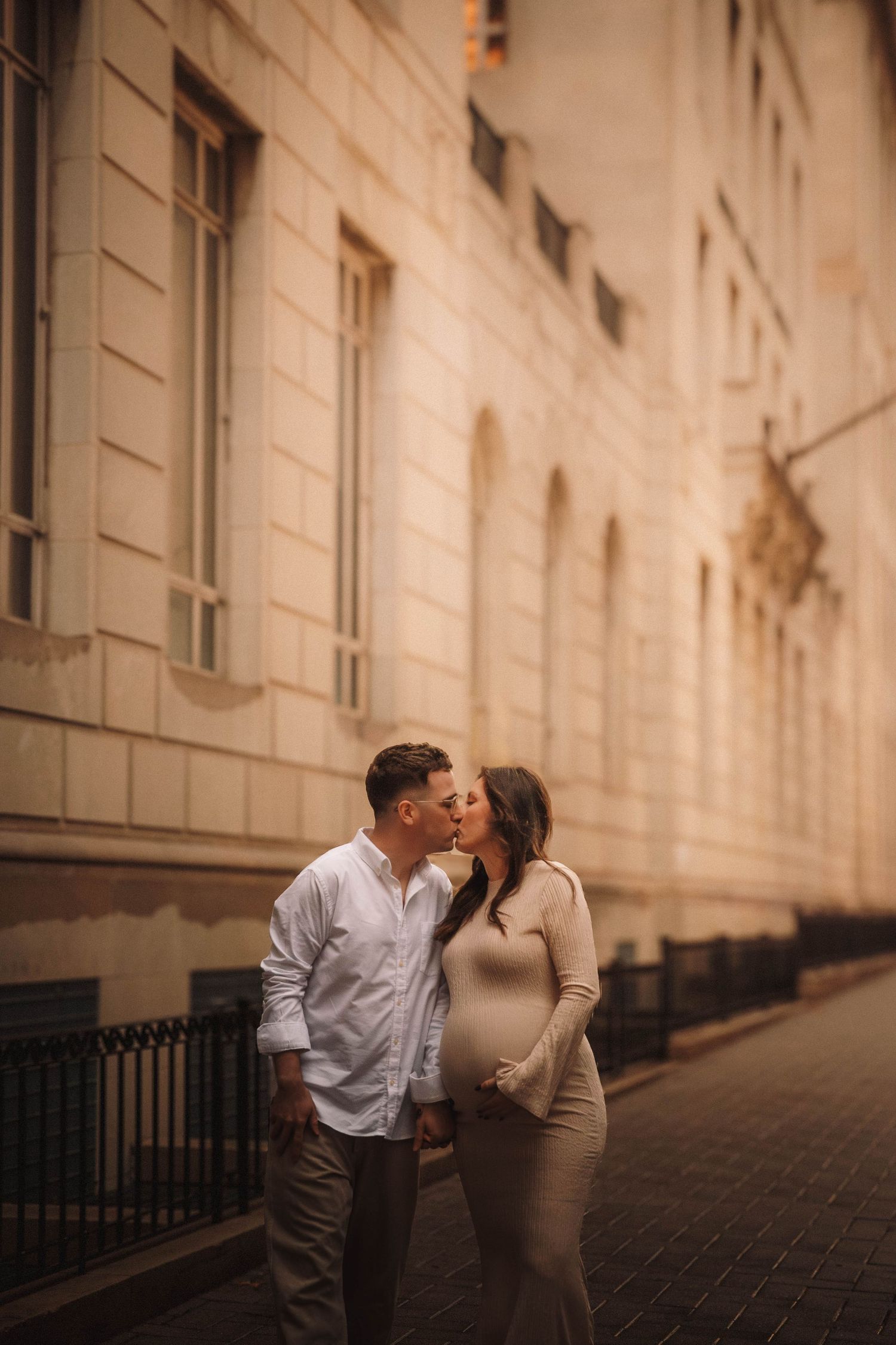 A couple shares a romantic kiss in the sepia-toned corridor of a beautiful historic building.