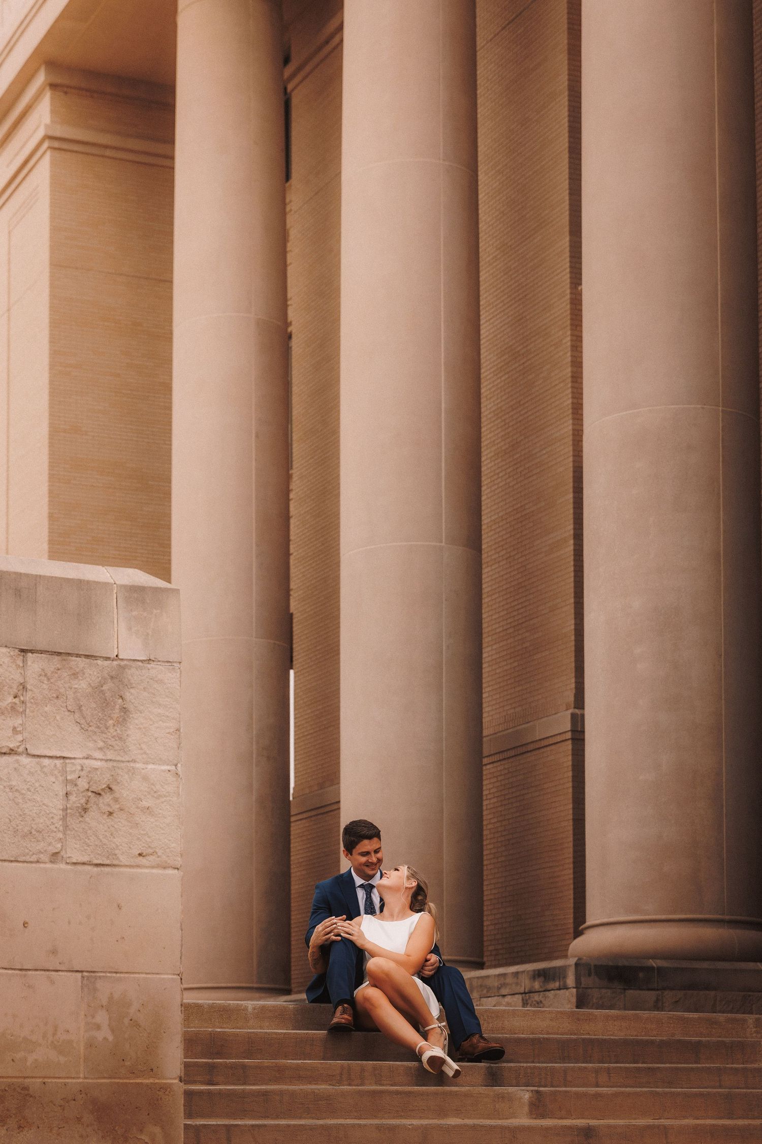 Romantic couple sitting between grand marble columns of a historic building captured in warm tones.