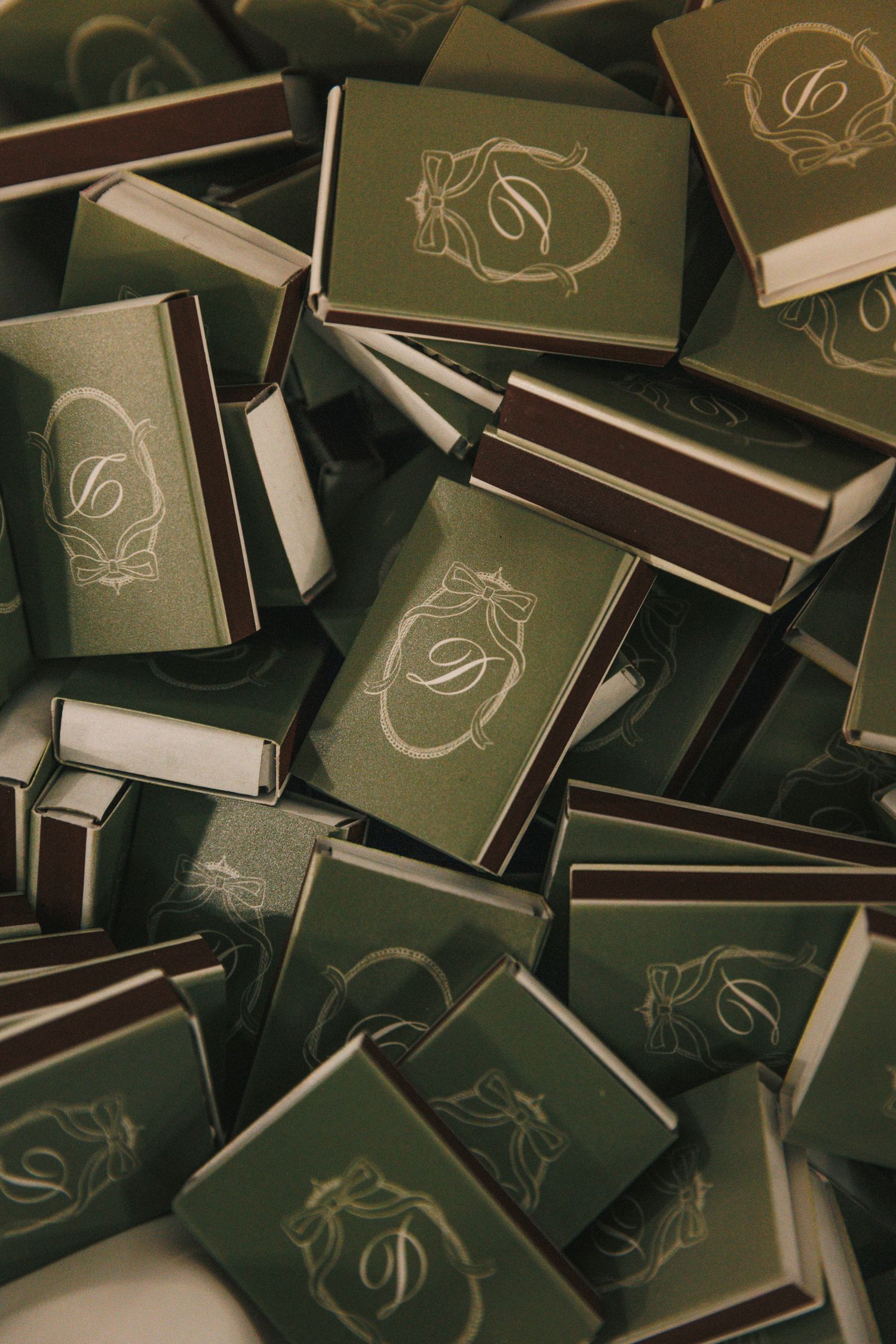 Collection of dark wedding matchbooks with elegant gold foil monogram designs scattered across surface.