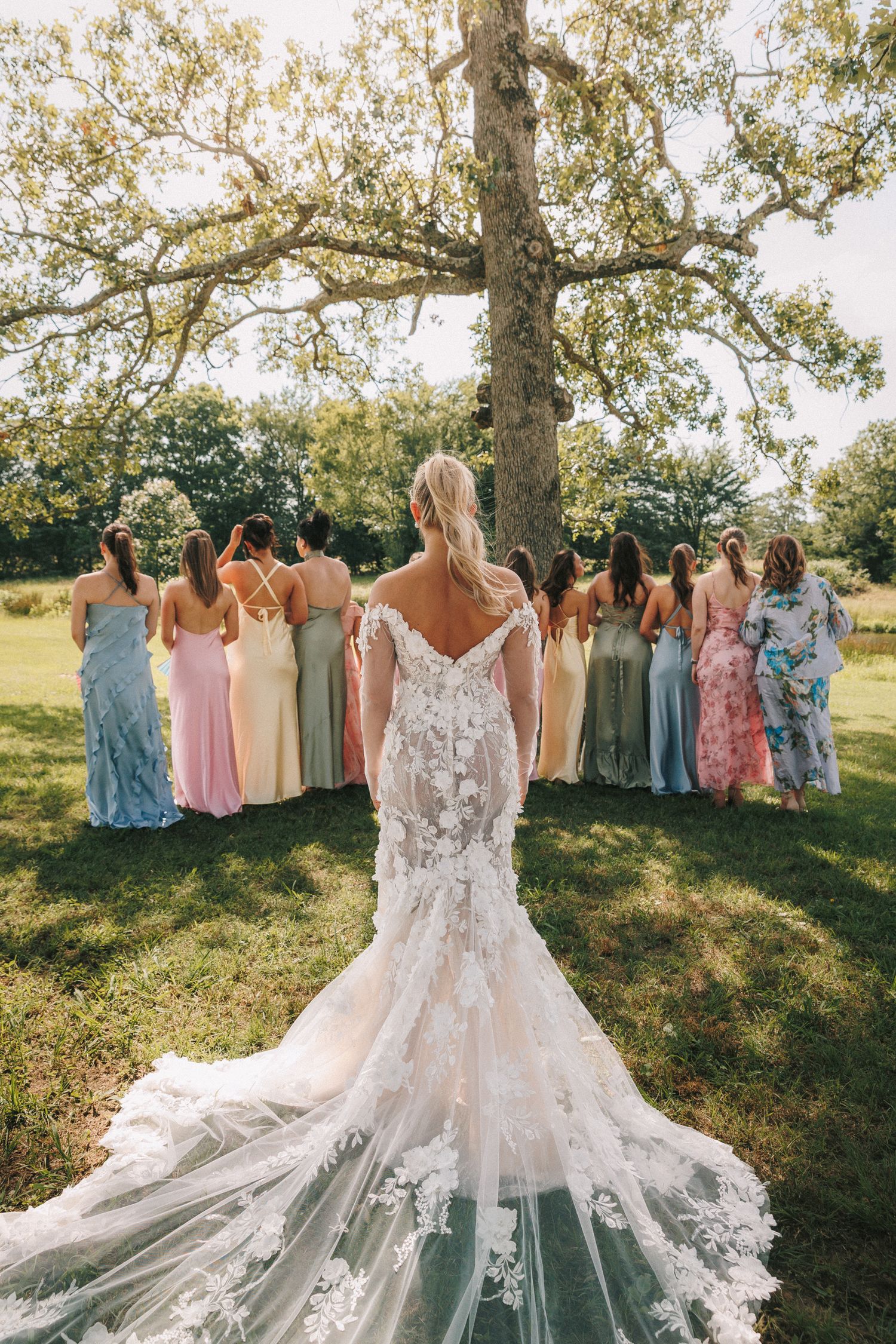 Elegant wedding gown with bridesmaids in pastel dresses gathered under blooming trees.