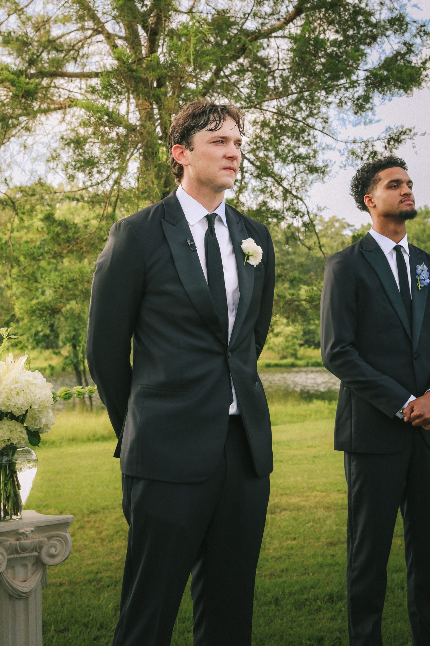 Groomsmen in black suits and ties standing in formation outdoors during wedding ceremony.