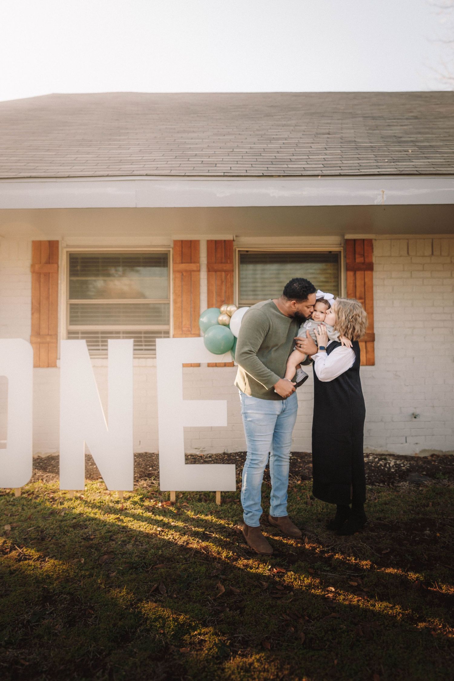 A series of four similar images show a couple embracing in front of a white brick wall at sunset.