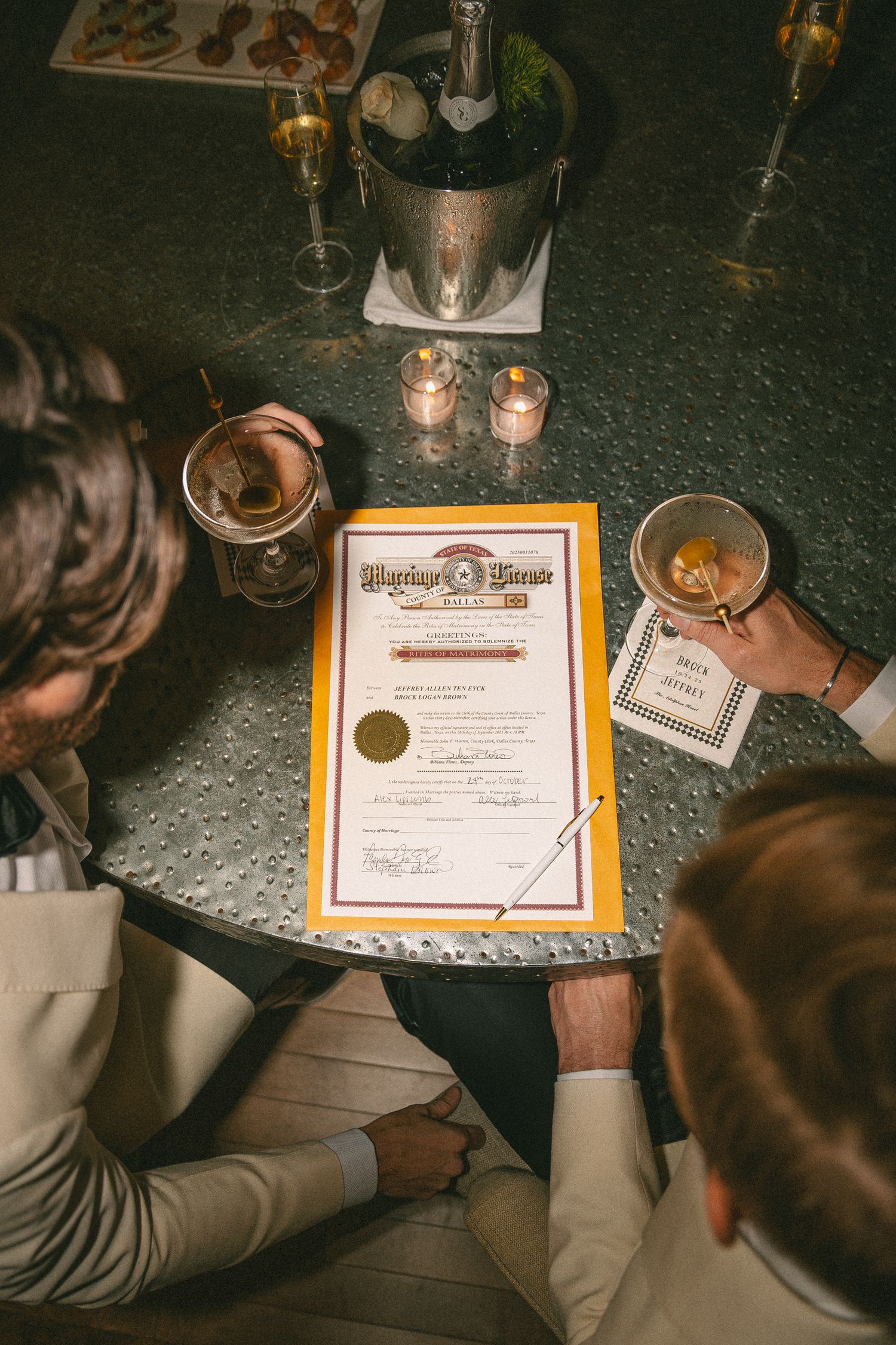 Two grooms review their marriage license certificate at a candlelit table with champagne.
