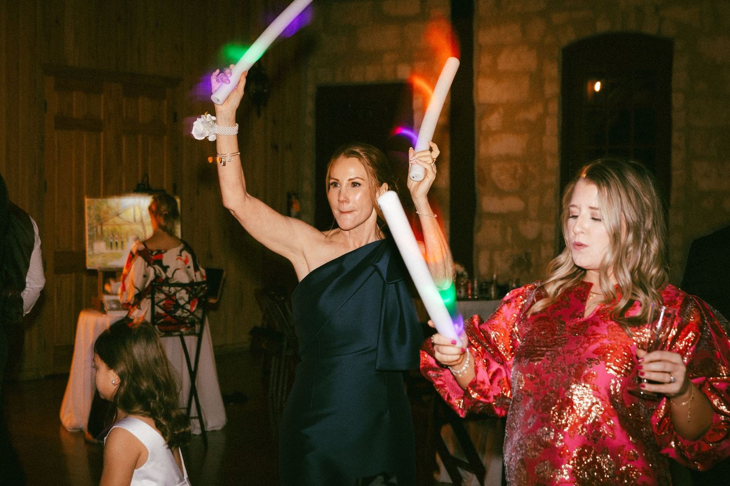 Wedding guests dancing with colorful glow sticks at a lively indoor reception.