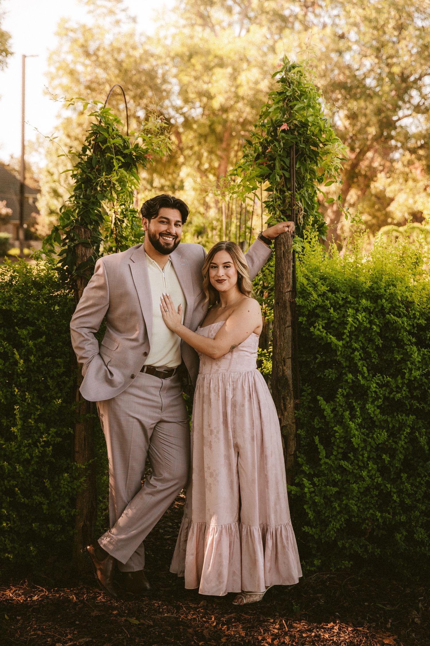 A romantic couple poses in a garden wearing coordinating beige outfits during golden hour.