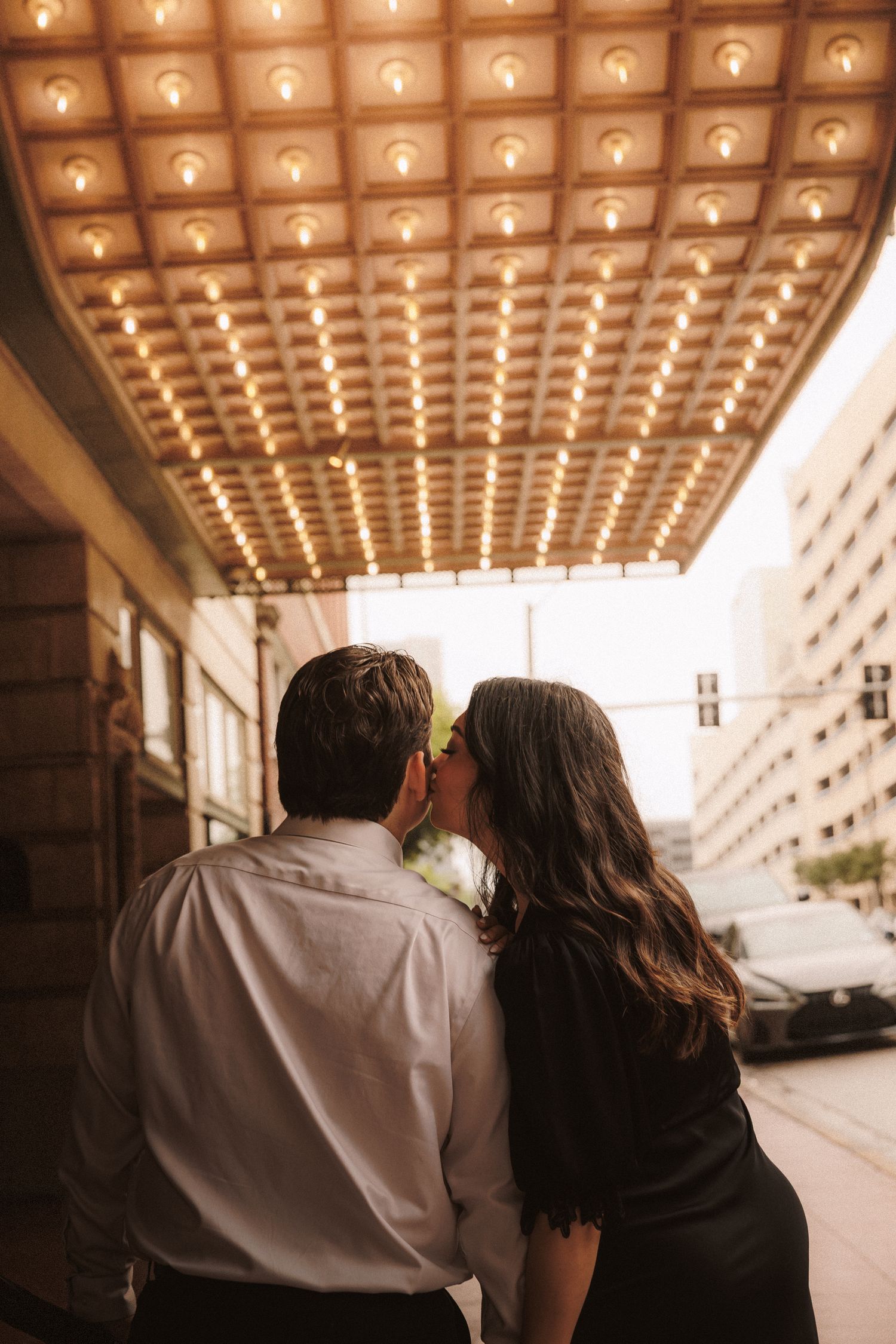 Couple sharing a romantic kiss under glowing marquee lights on a city street.