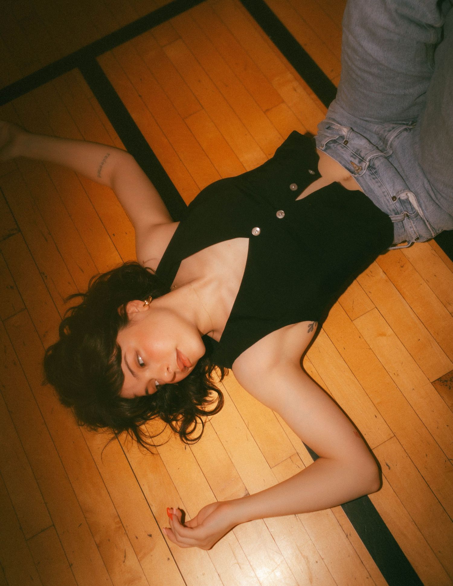 A person lies gracefully reclined on a polished wooden floor in dramatic lighting.