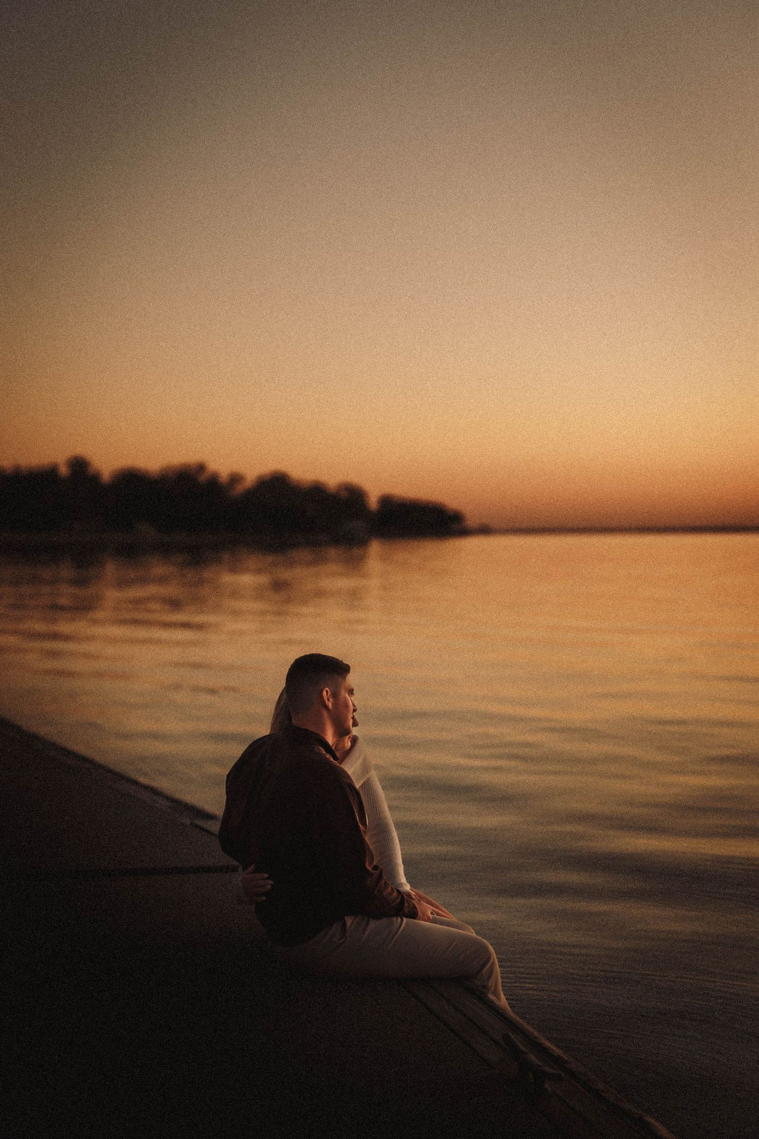Silhouettes of a couple resting on a waterfront dock during a peaceful sunset.