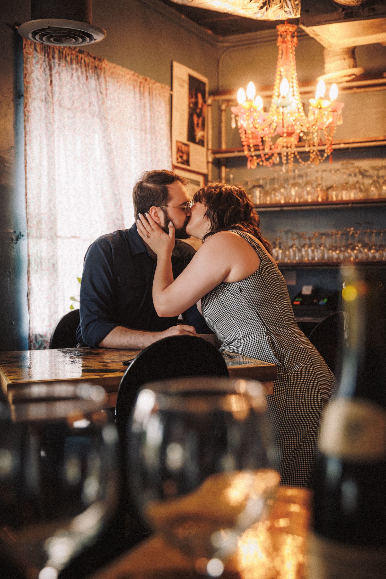 Romantic scene in dimly lit restaurant with chandeliers and wine glasses on table.