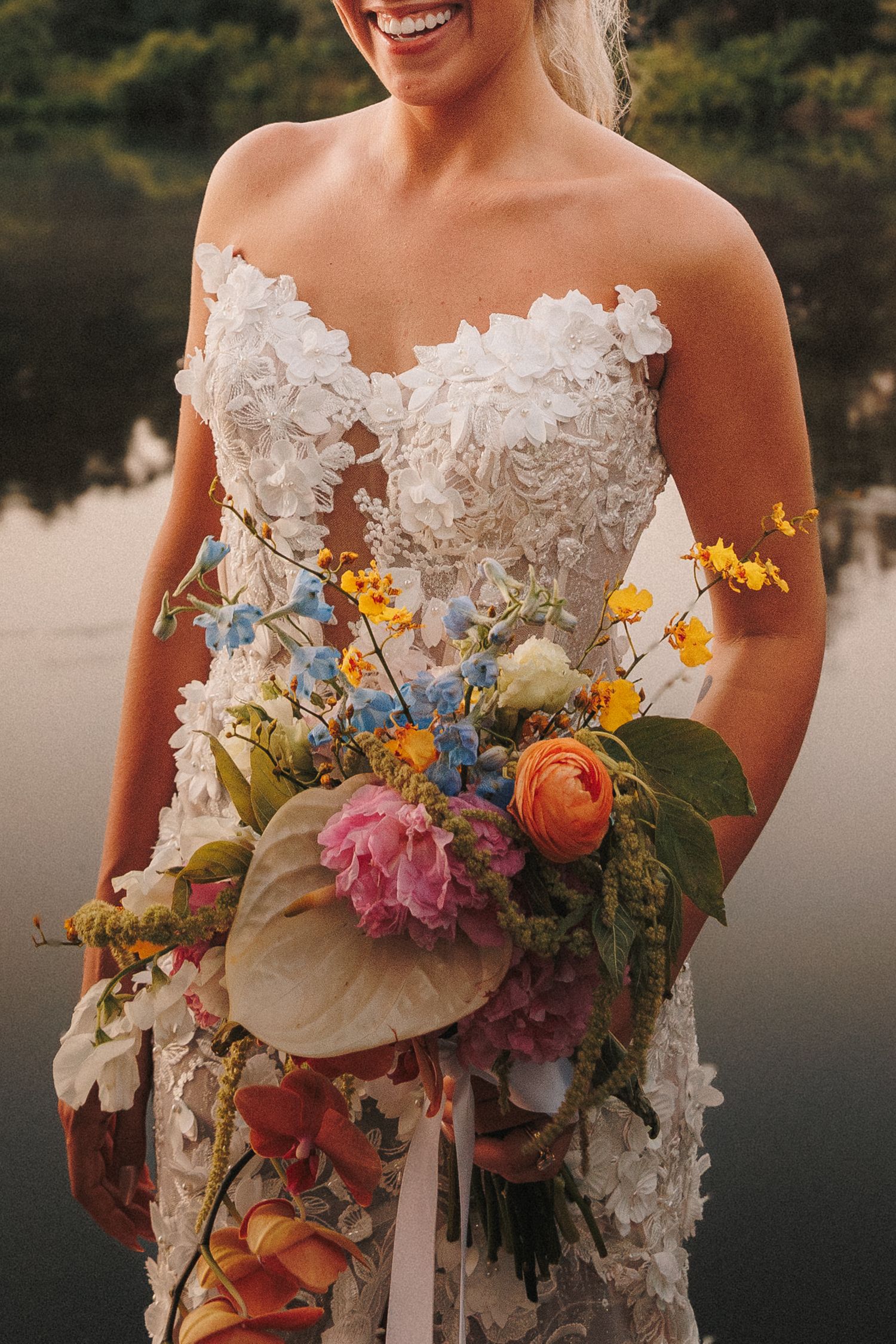 A vibrant bridal bouquet features colorful wildflowers, roses, and delicate blooms against a lace dress.