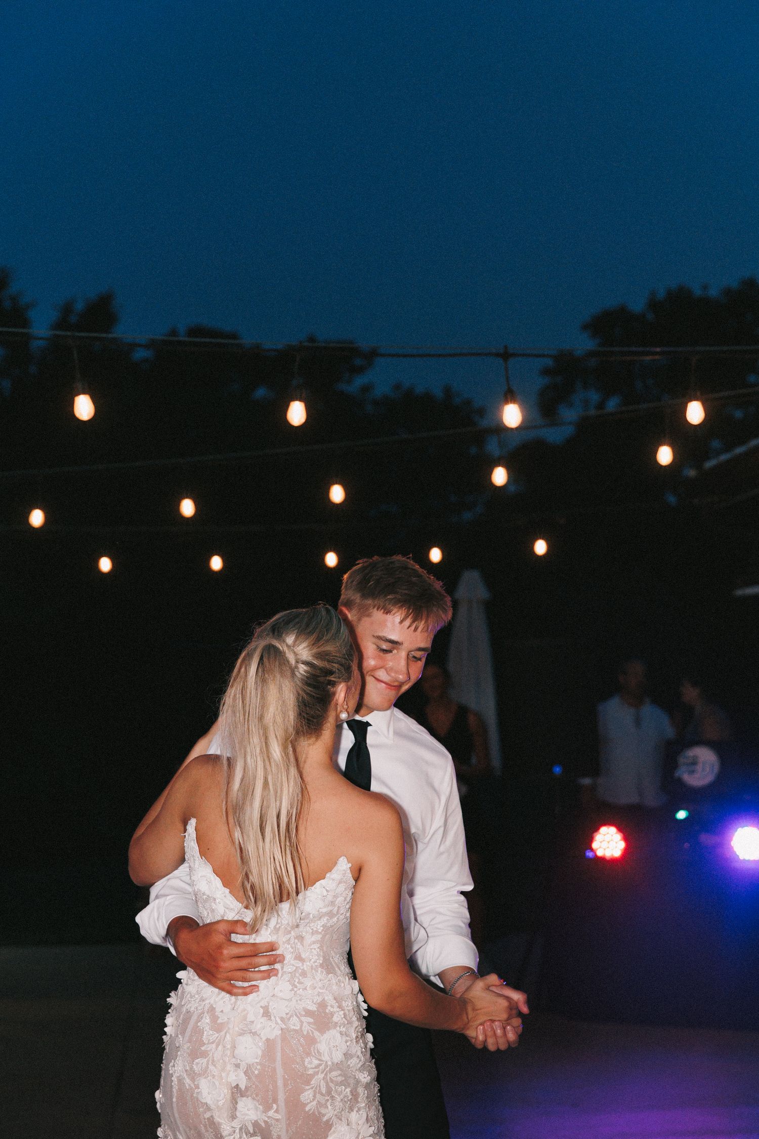 Wedding couple dancing under string lights during evening reception.
