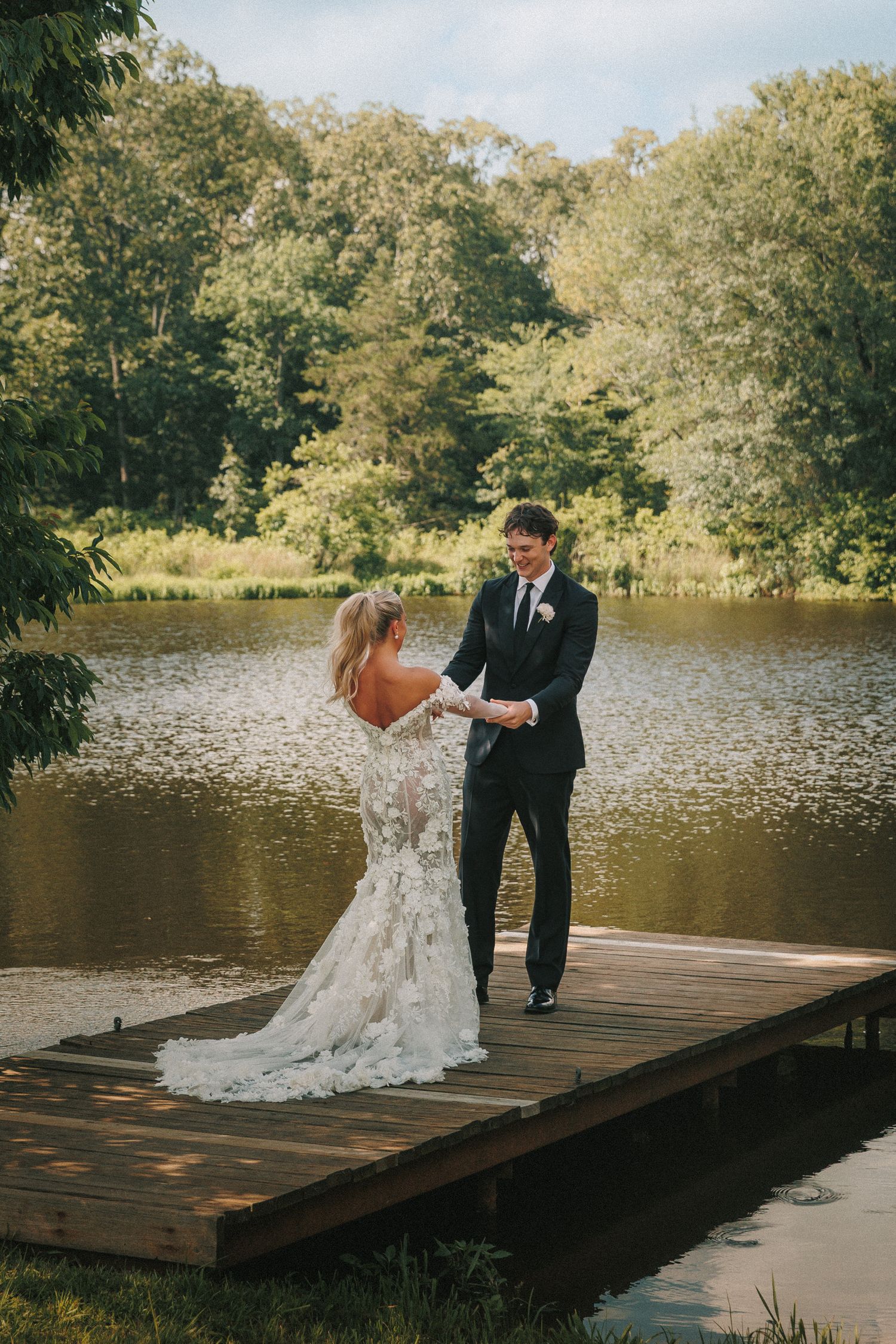 Wedding couple dances together on rustic lakeside dock during outdoor celebration.