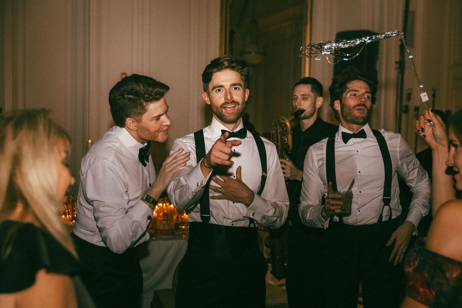 Groomsmen in suspenders and bow ties celebrate at wedding reception party.