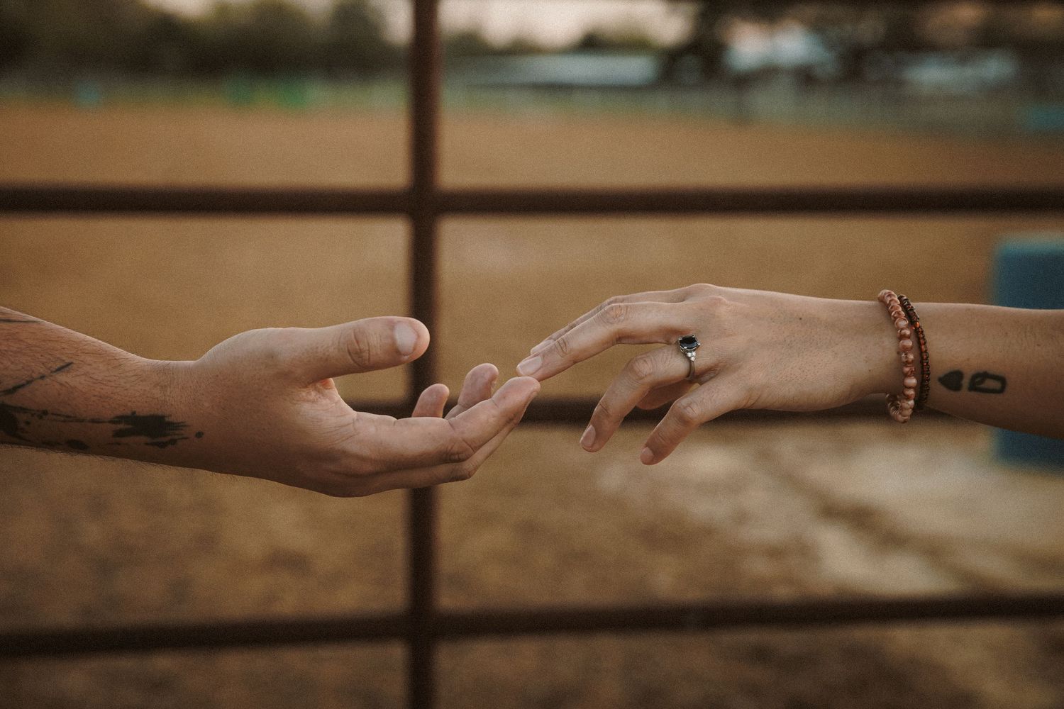Close-up of tattooed hands reaching toward each other, woman wearing engagement ring.