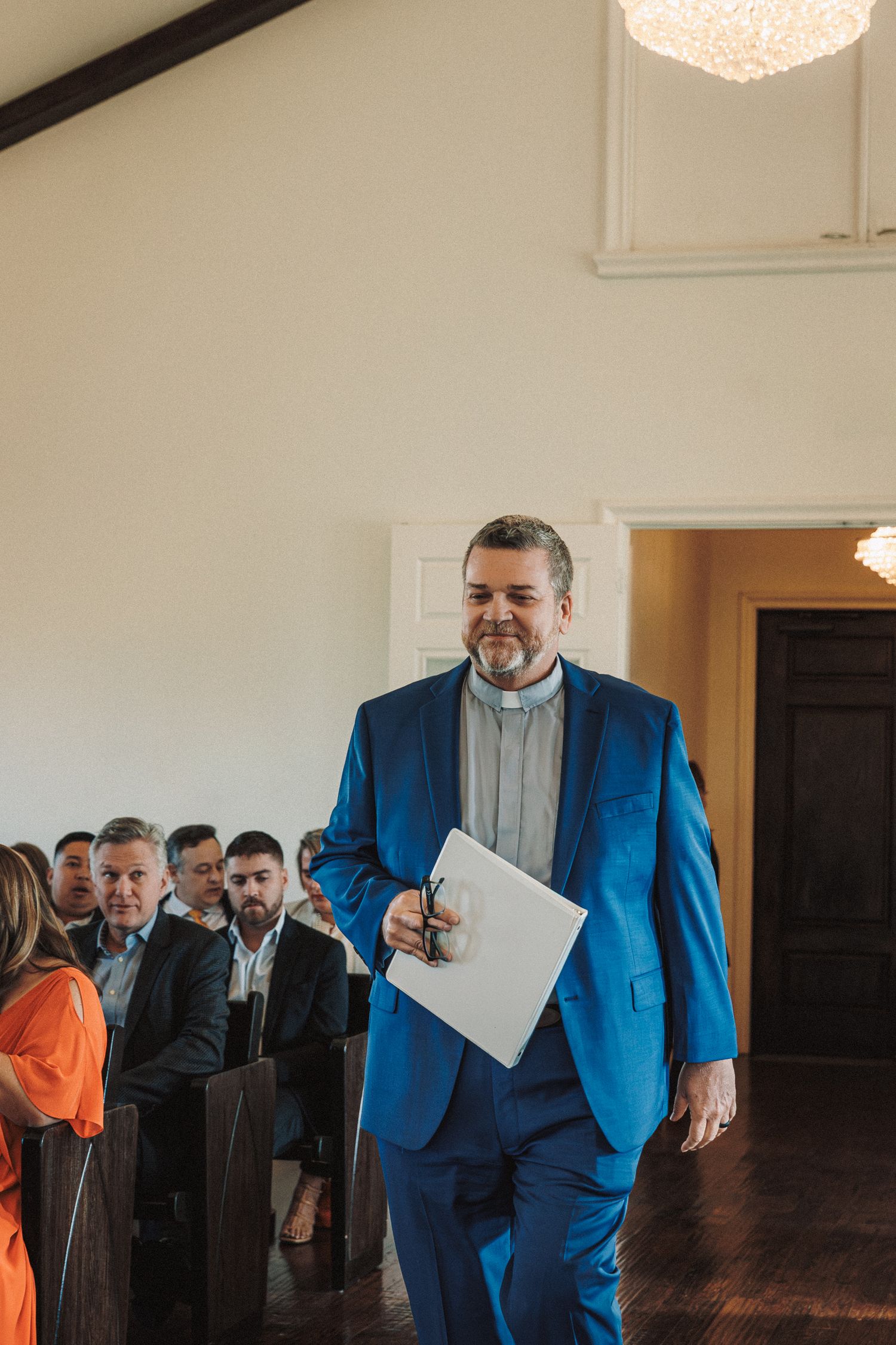 Officiant in blue suit walking into chapel holding ceremony booklet before wedding.