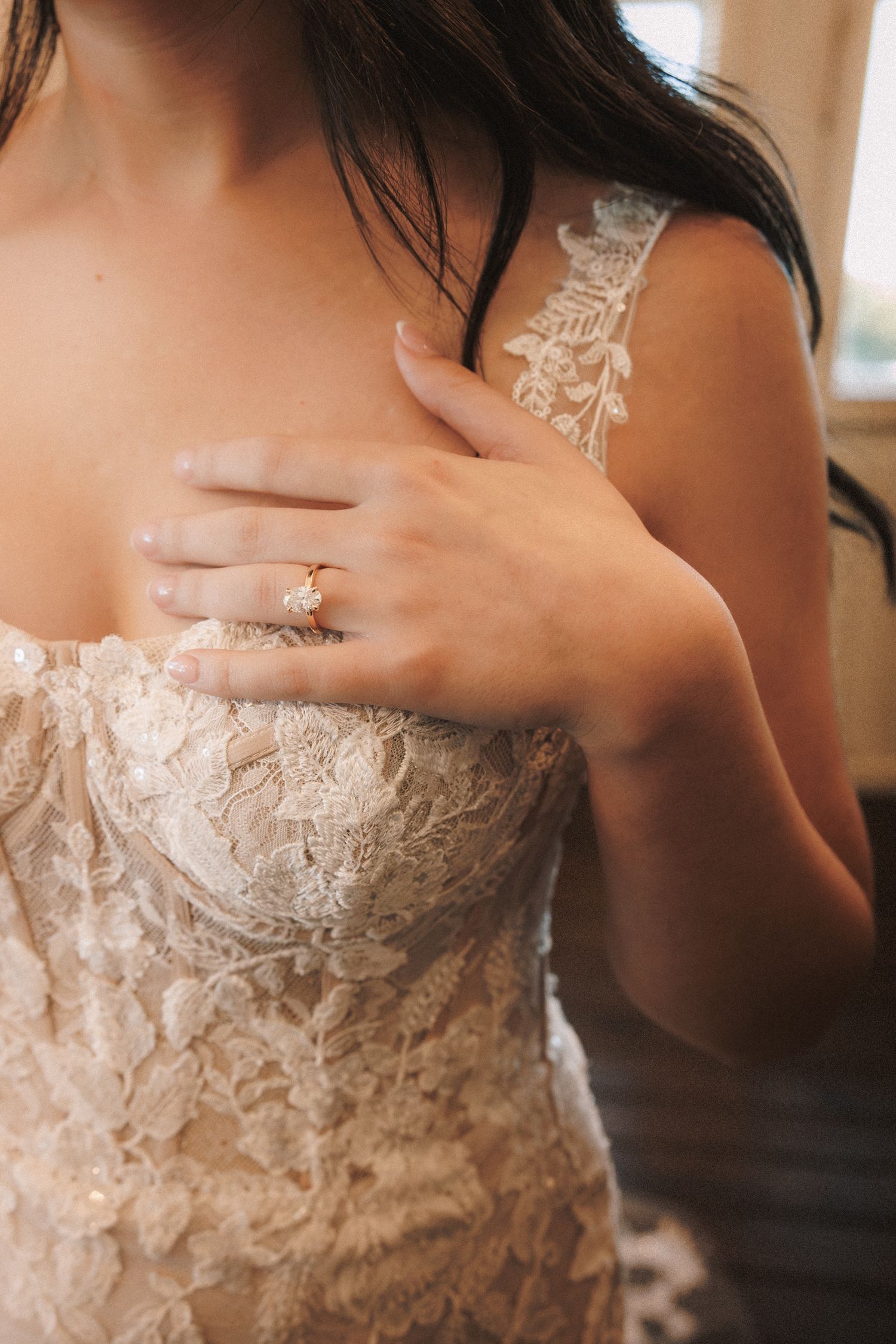 Close-up of a bride in a lace wedding gown with a gold diamond engagement ring on her hand.