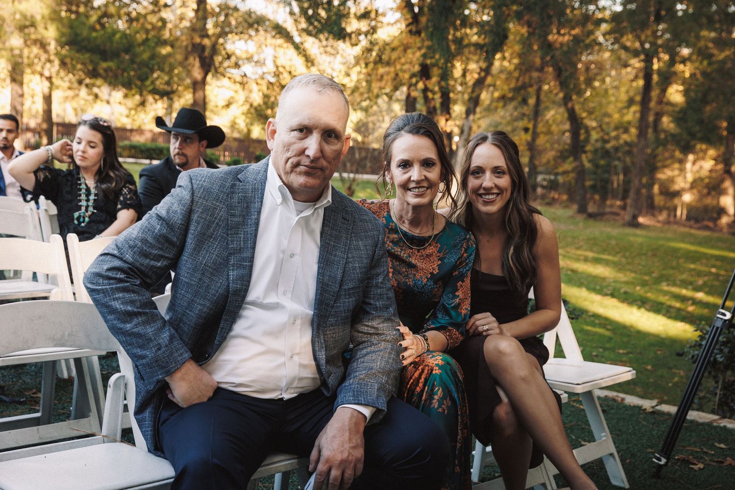 Three wedding guests smiling for a photo outdoors at a garden wedding ceremony.