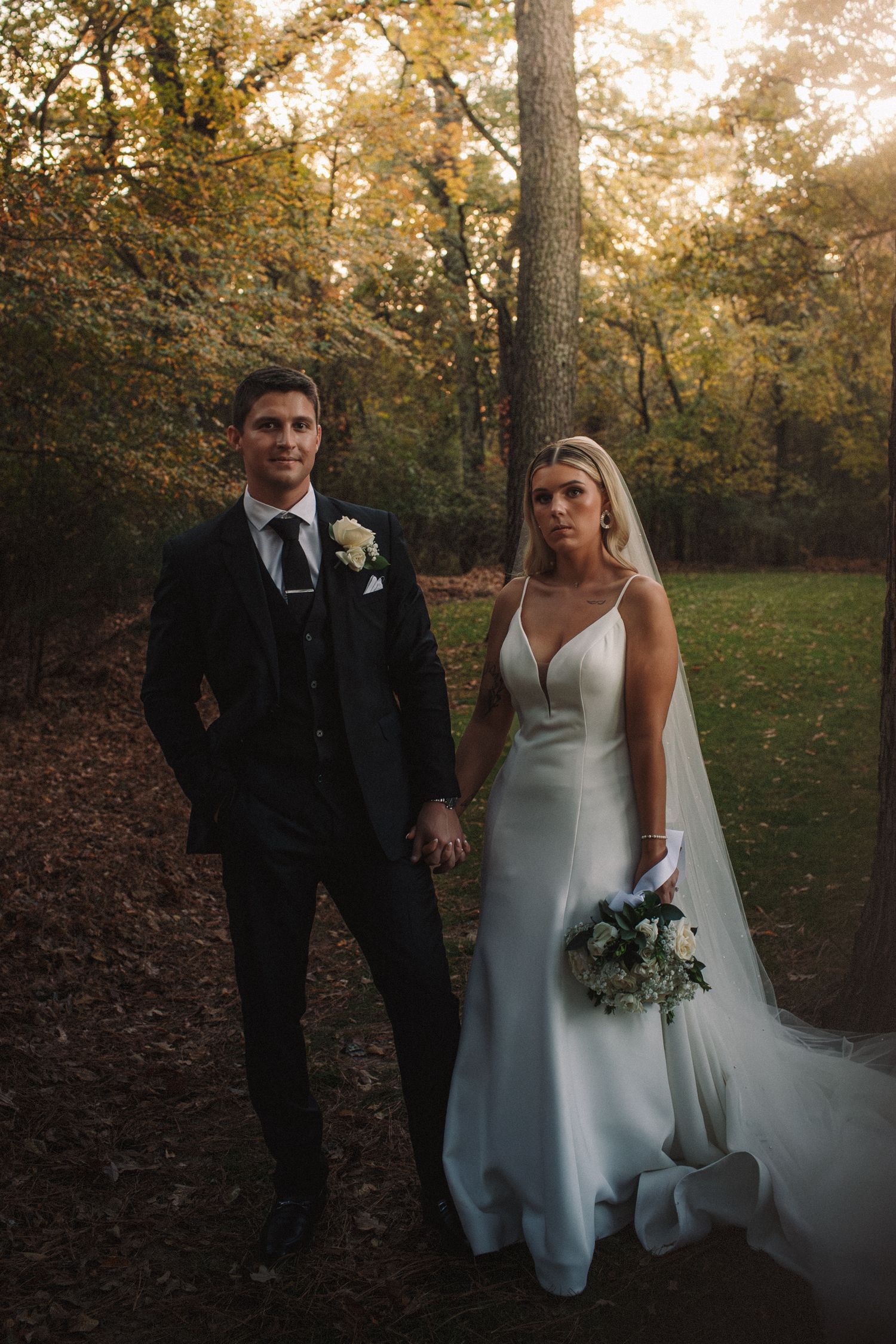 Bride and groom holding hands while posing together in an autumn forest during their wedding.