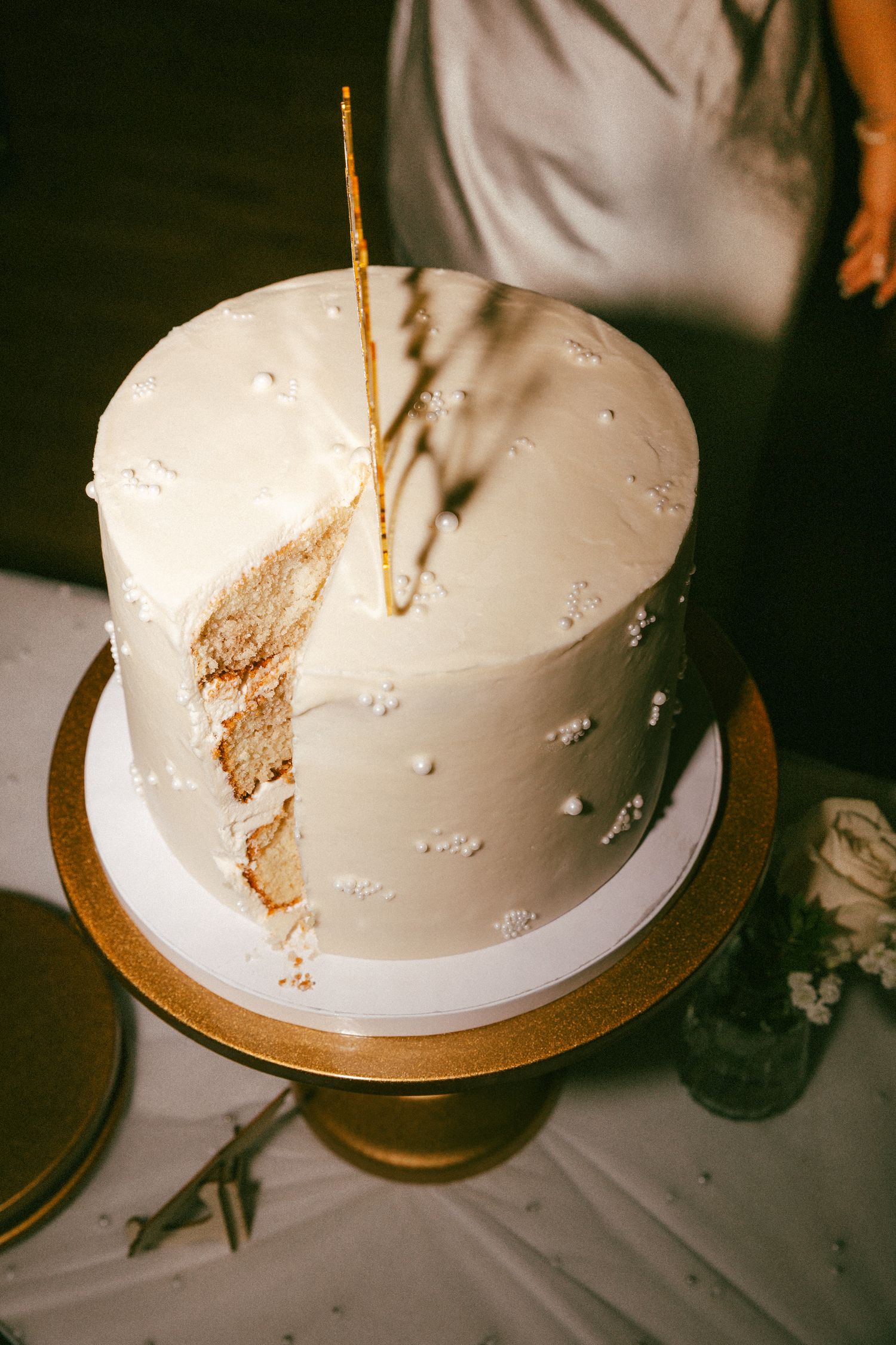 An elegant single-tier white wedding cake with gold accents on a gold cake stand.