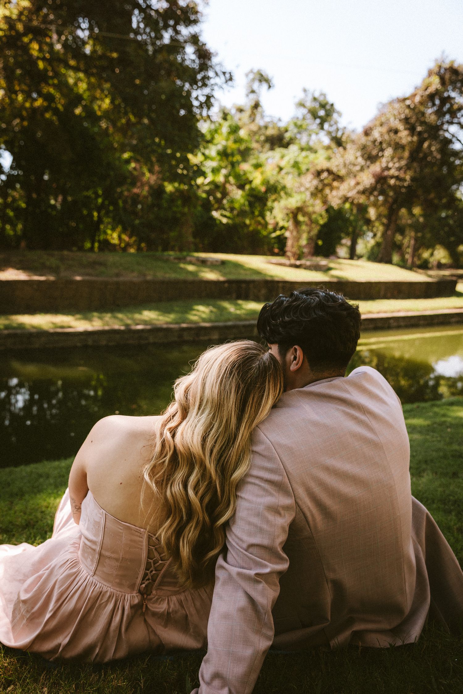 A couple sits close together on a bench in a peaceful garden setting during golden hour.