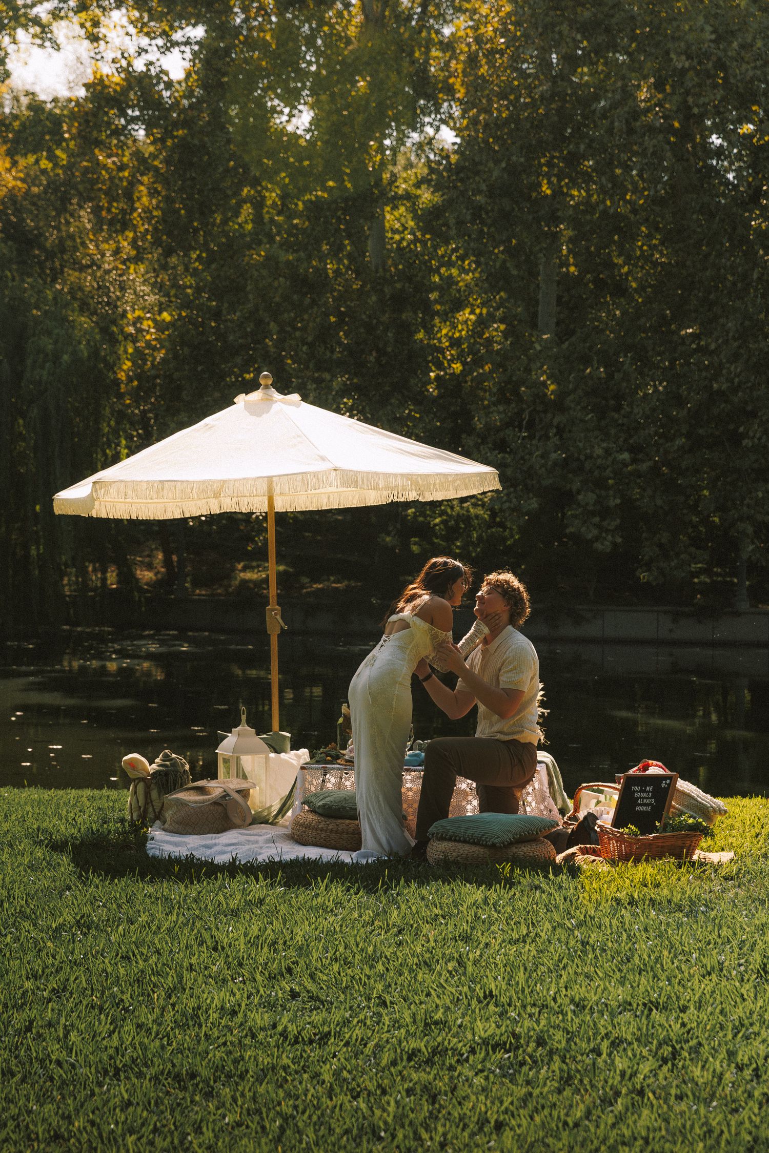 Couple relaxing on grass under white parasol umbrella in park during golden sunset.