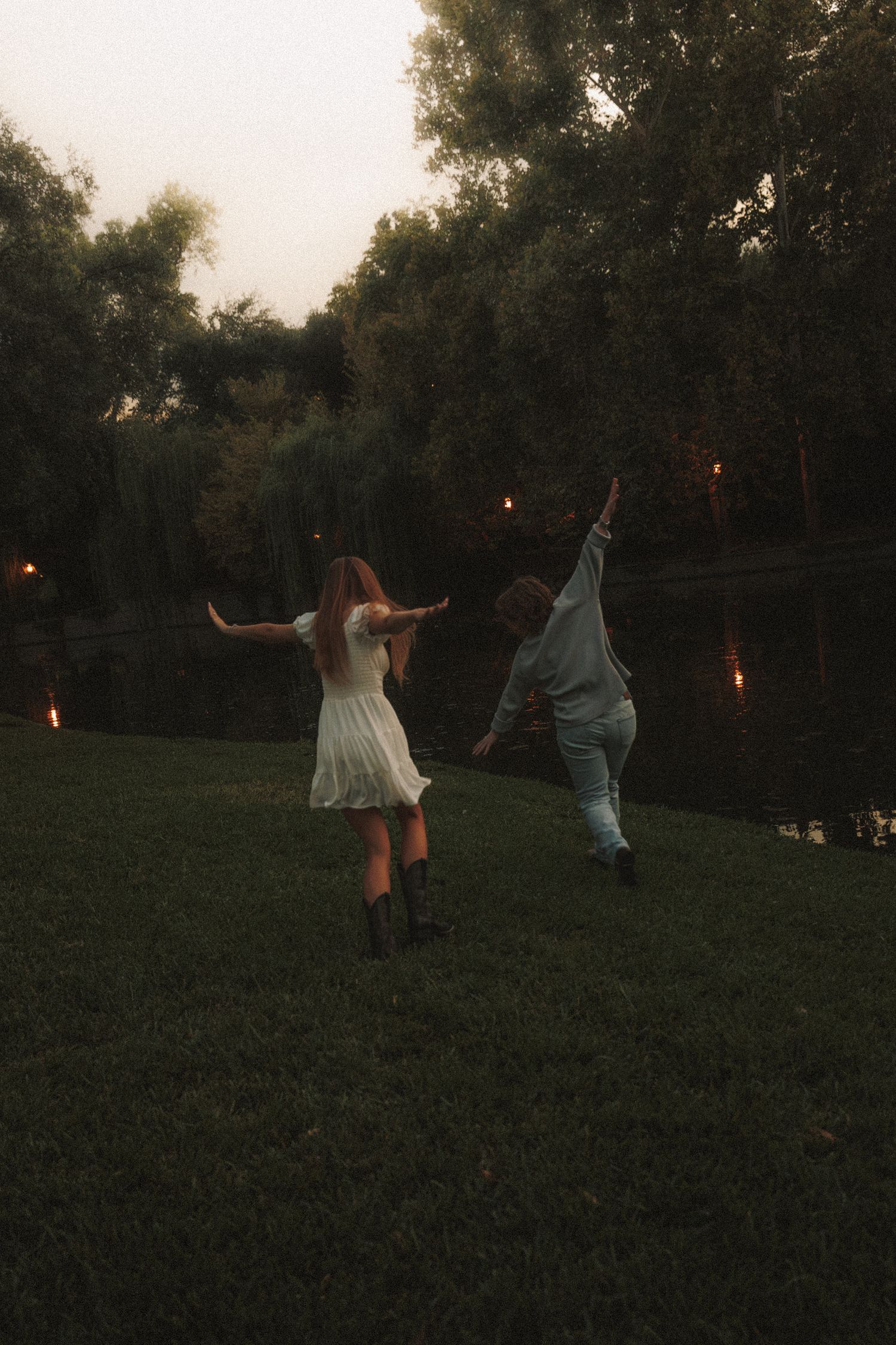 People dance joyfully in a grassy field at dusk with trees in the background.