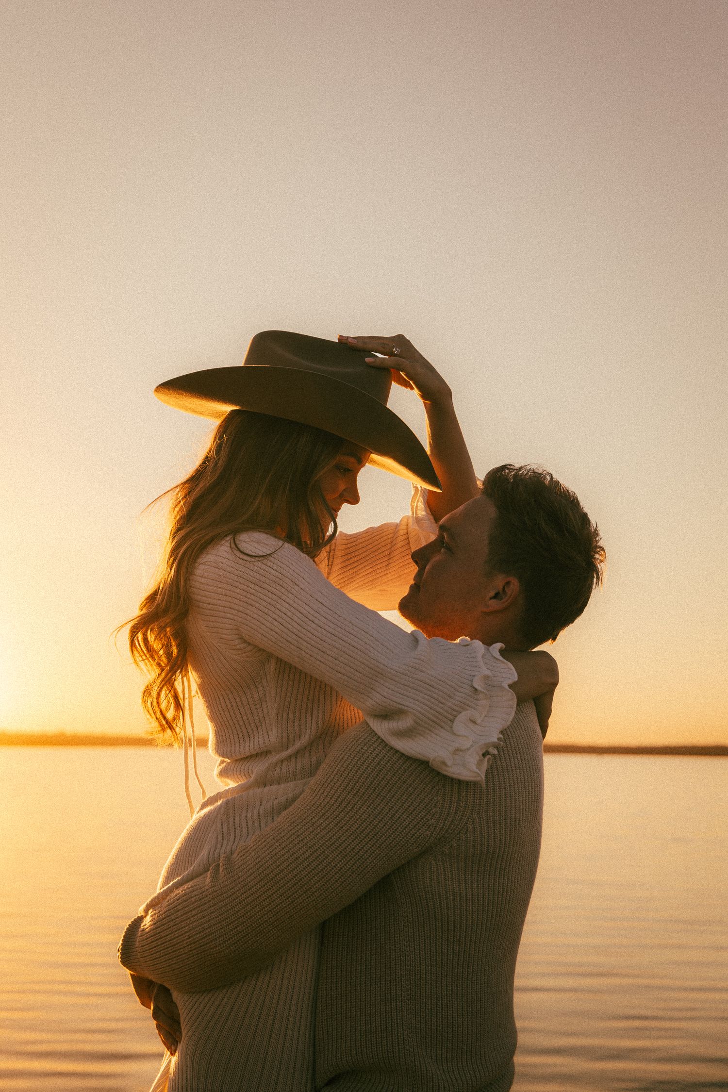 A romantic couple embraces on a beach during golden hour sunset with ocean waves in the background.