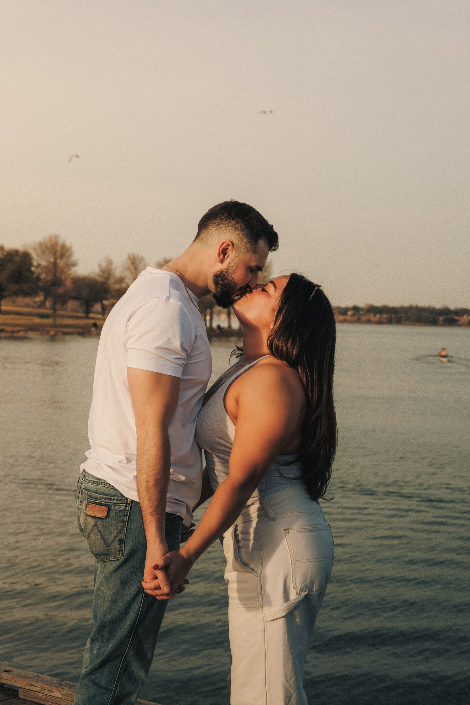 Romantic couple sharing an intimate moment by the waterfront during golden hour with boats in the background.