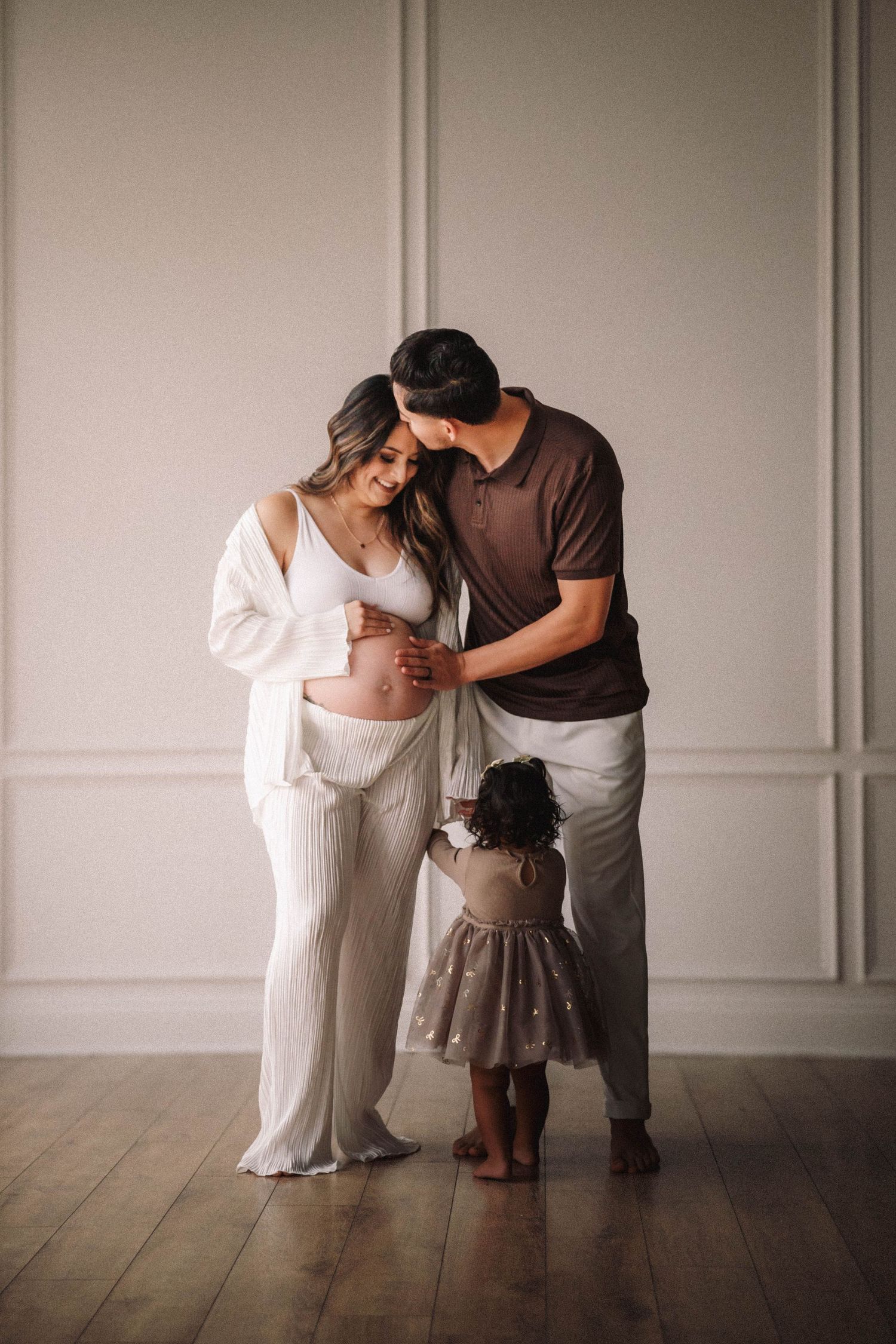 Silhouetted figures in white and brown clothing create a tender moment against light walls and wooden flooring.