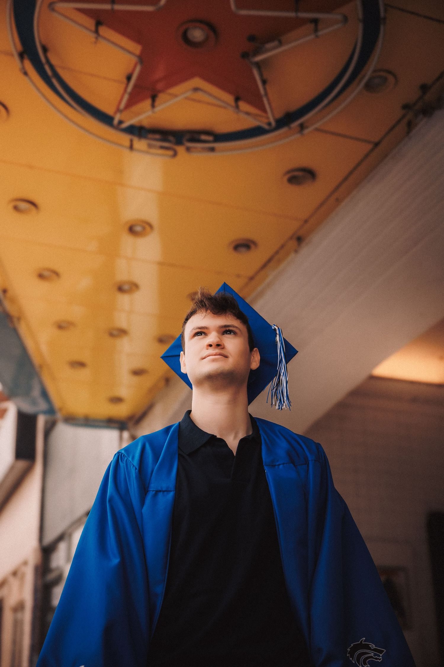 Figure wearing a bright blue graduation gown and cap against an amber-colored background.