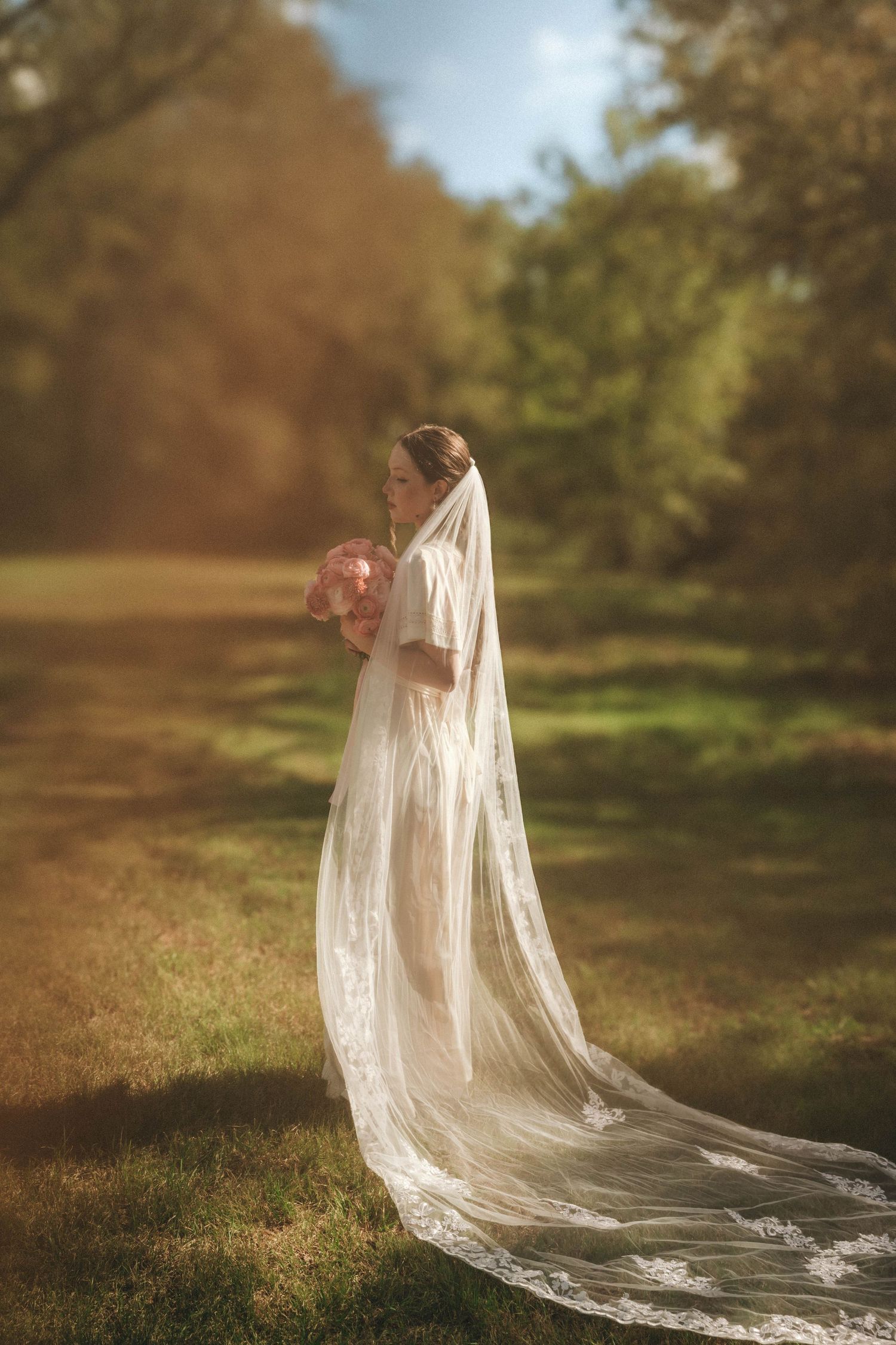 A long flowing wedding veil trails behind a figure in a pastoral outdoor setting at sunset.