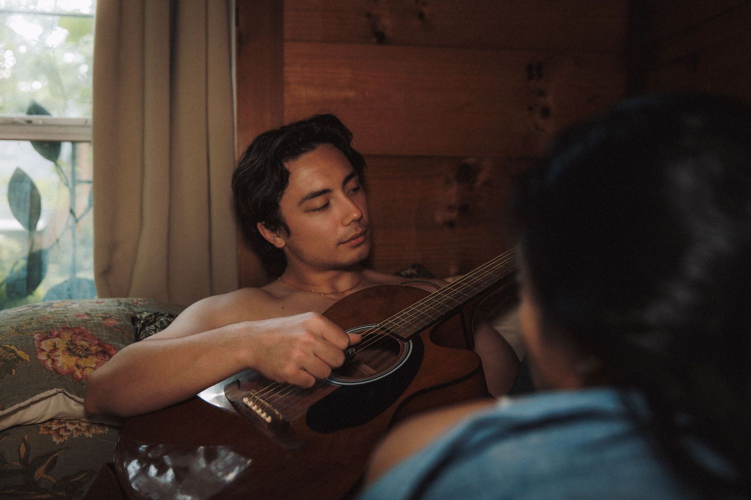 A person relaxes on a couch while strumming an acoustic guitar in a cozy room with natural lighting.