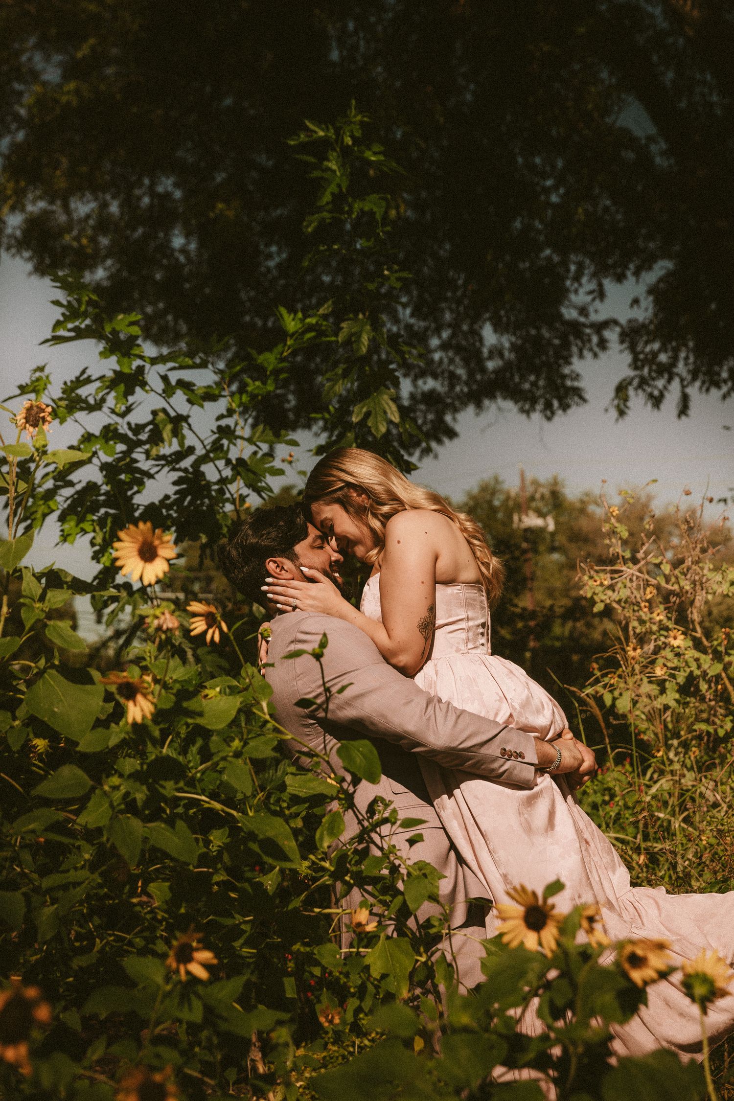 A romantic couple embraces in a sunlit meadow surrounded by blooming wildflowers at golden hour.
