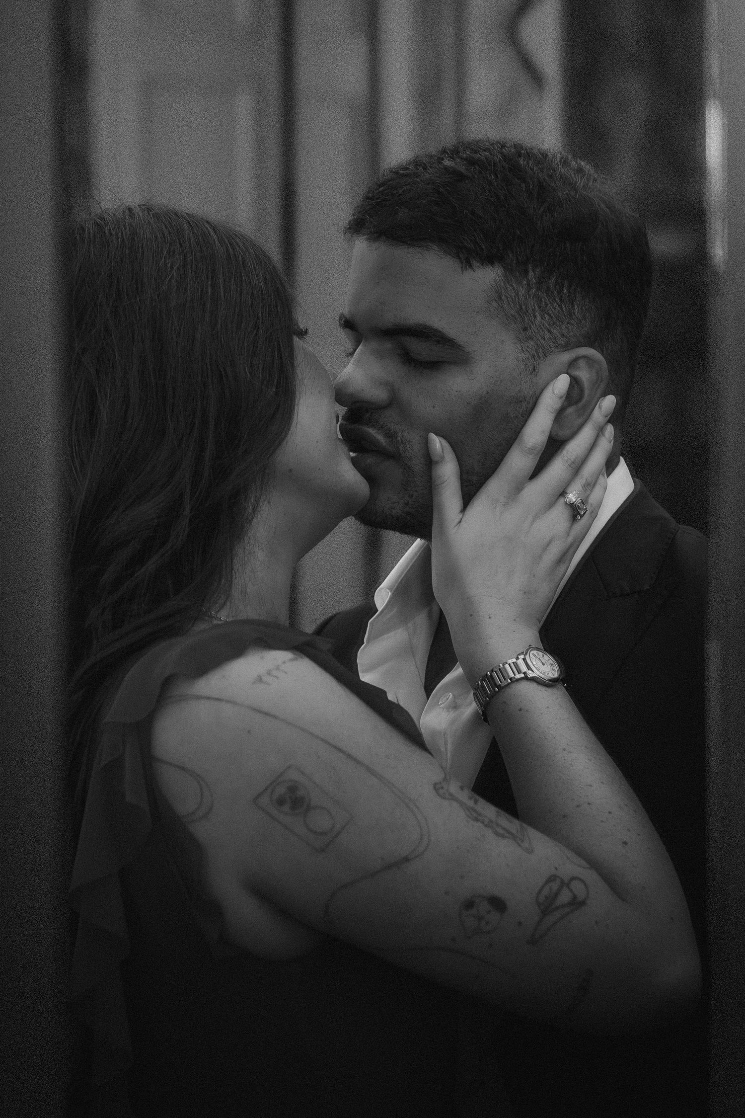 Black and white photo of a couple sharing a romantic moment, woman with tattoos gently holding mans face.