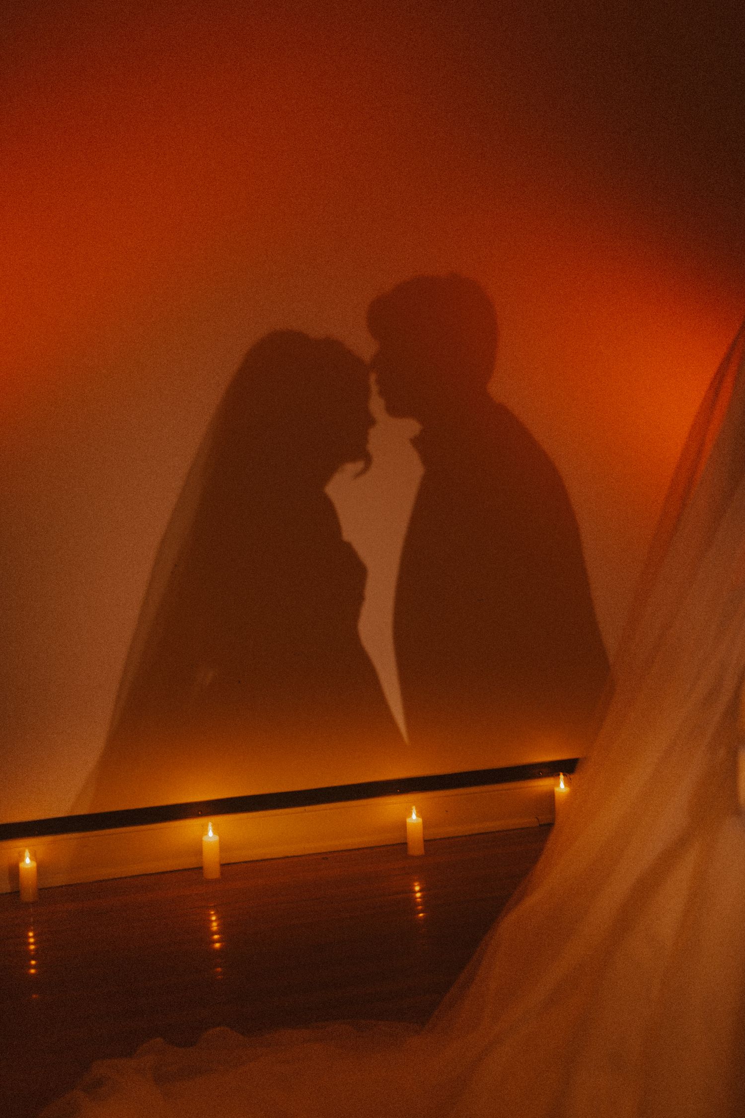 Silhouette of bride and groom facing each other cast on wall with candles glowing below.