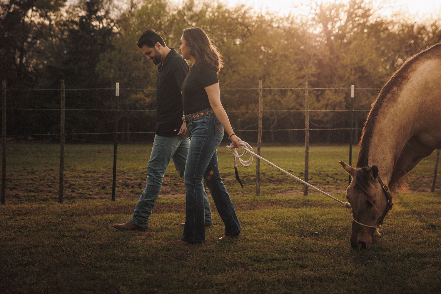Couple walking together leading a horse on a rope in a warm sunset farm setting.