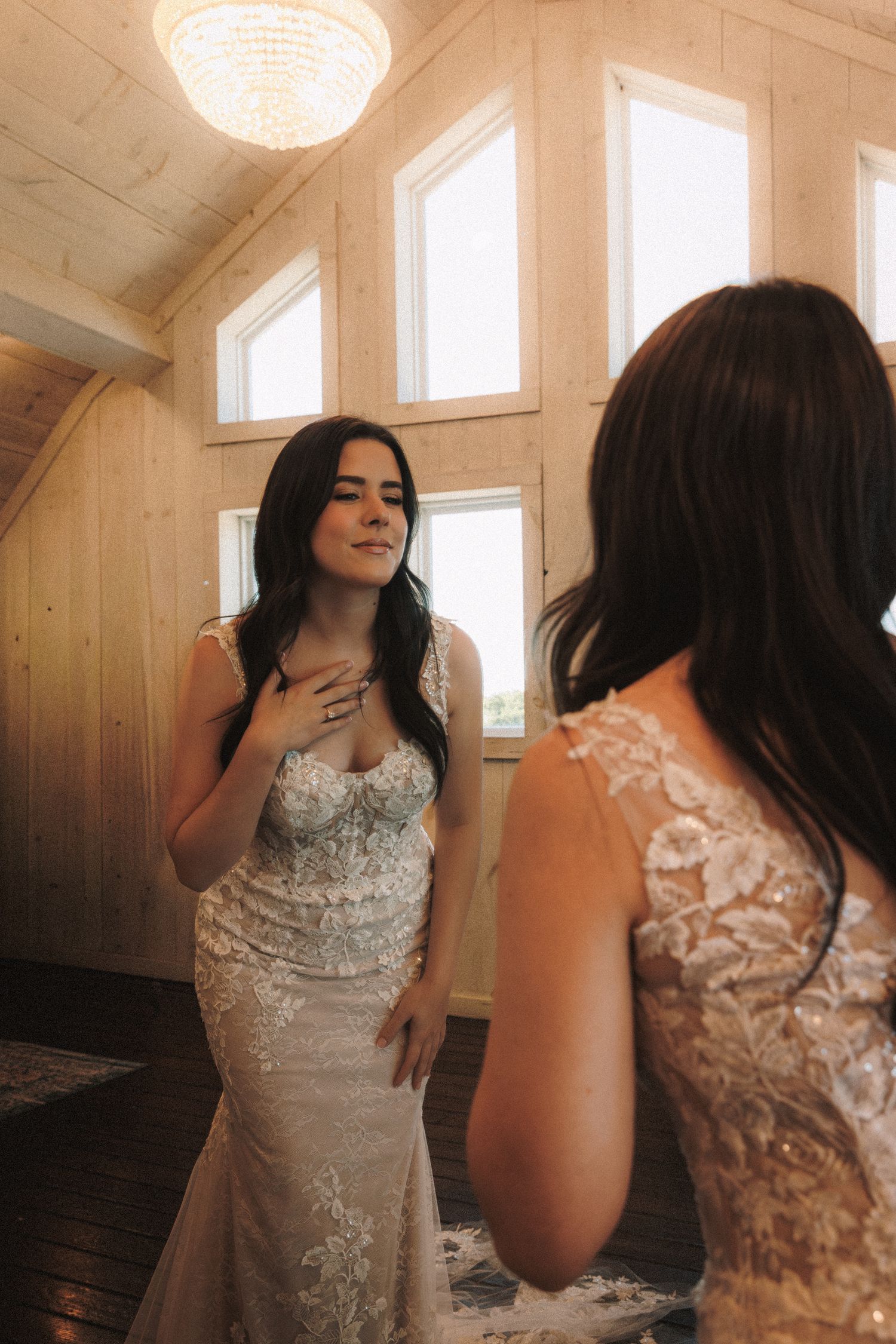 Bride in a lace mermaid wedding dress admiring herself in a mirror with a chandelier above.