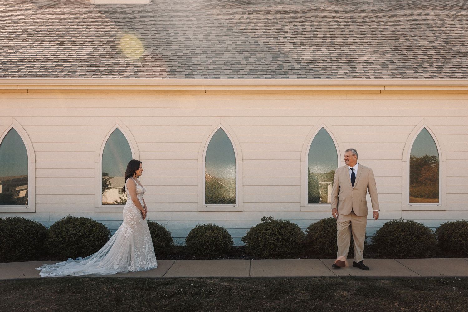 Bride and groom share a first look moment outside a white chapel at golden hour.