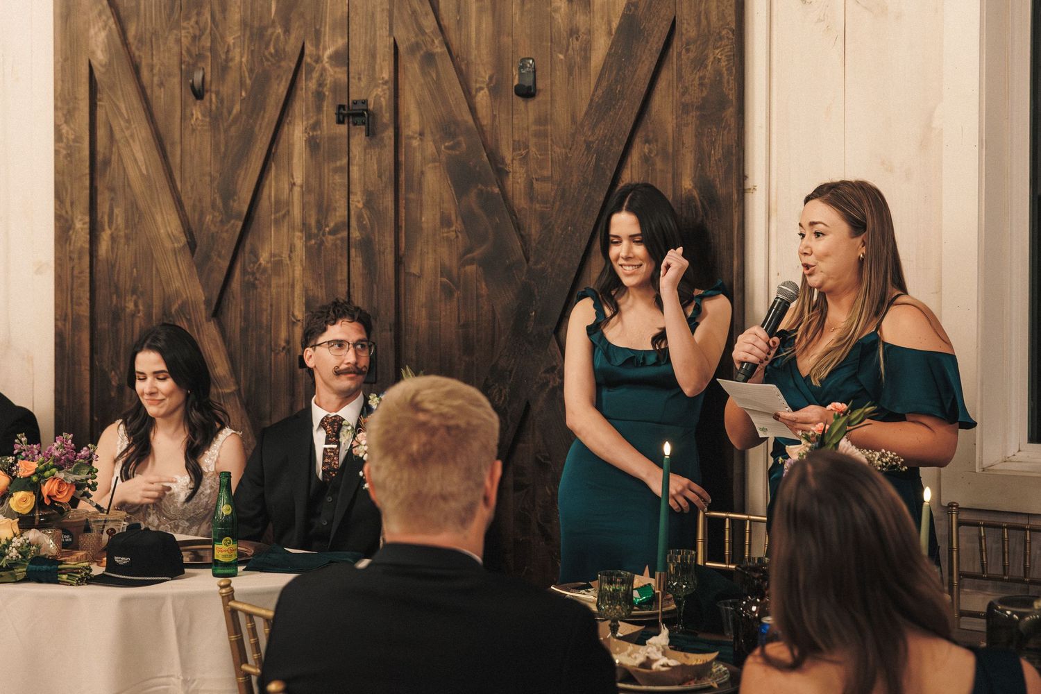 Bridesmaid delivers heartfelt speech at wedding reception near rustic barn wood doors.