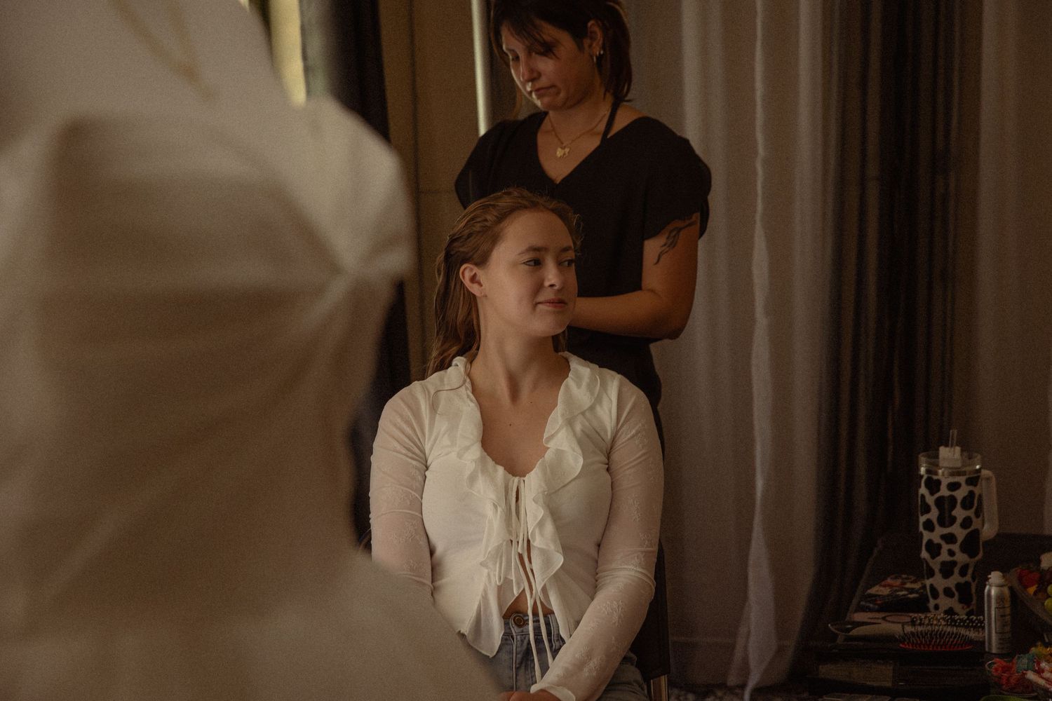 Bride getting hair styled by makeup artist before wedding ceremony in softly lit room.