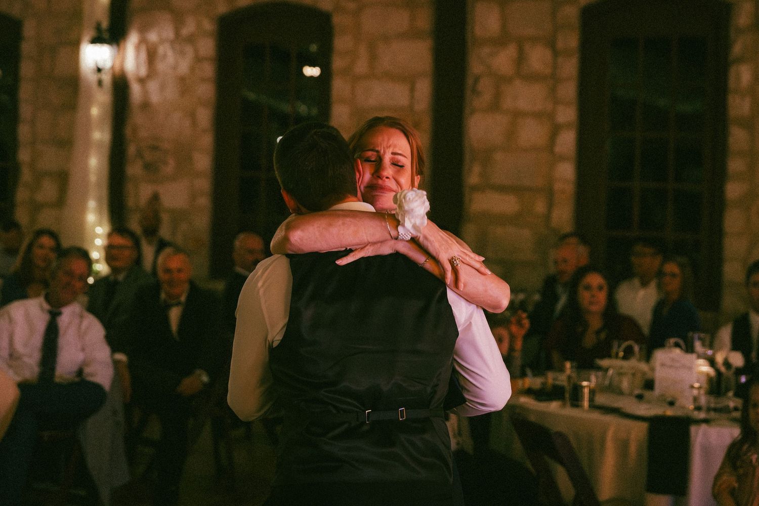 Groom shares an emotional mother-son dance in a warmly lit stone reception venue.