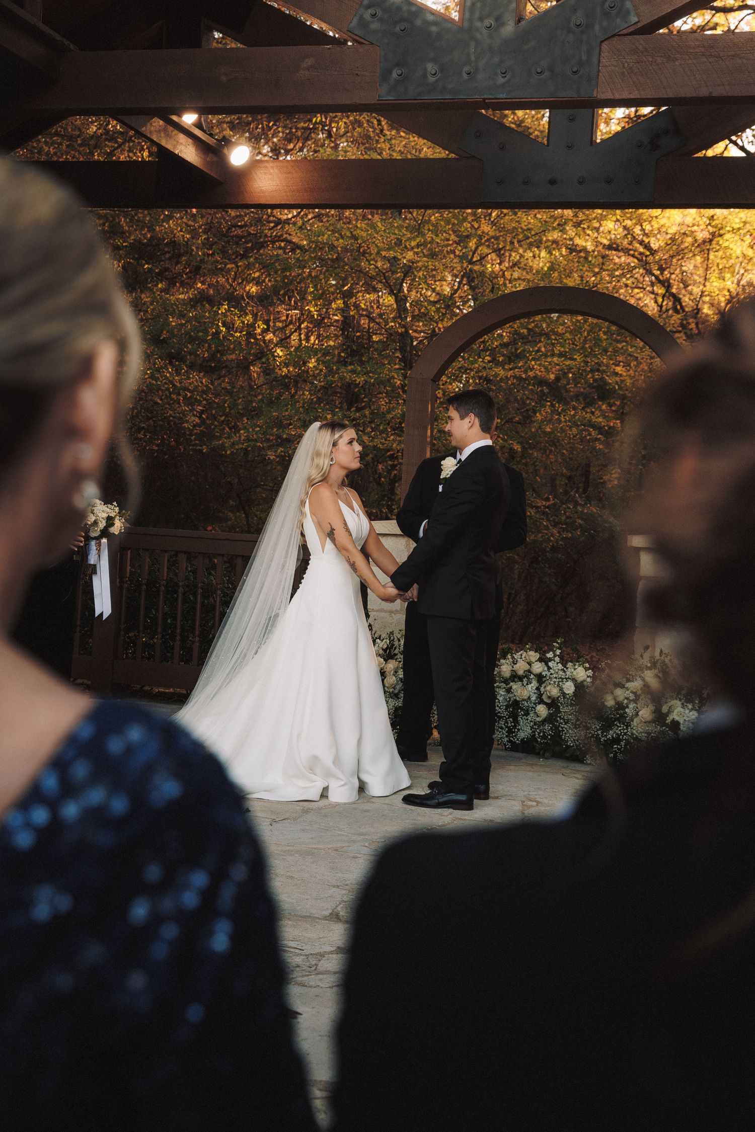 Bride and groom holding hands at altar under wooden pergola during outdoor wedding ceremony.