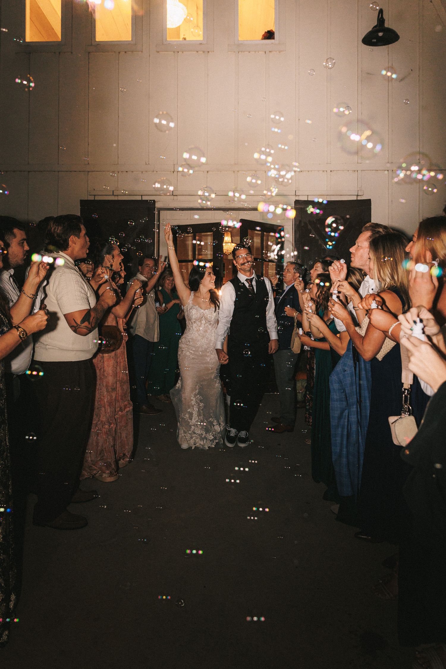 Bride and groom exit through a joyful bubble send-off surrounded by cheering guests.